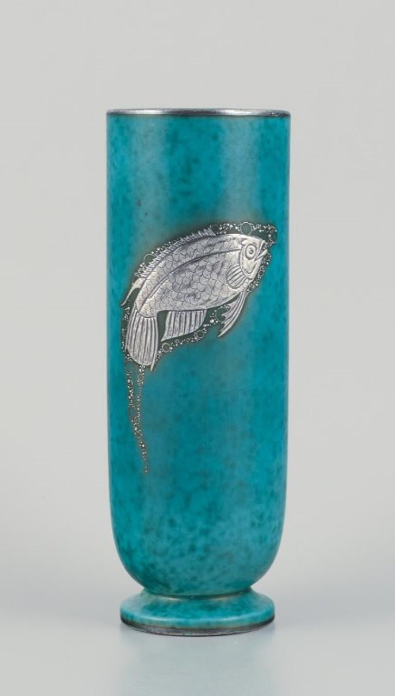 Wilhelm Kåge (1889-1960) for Gustavsberg, Sweden.
Art Deco ceramic vase with silver fish motif decoration.
From the Argenta series.
1940s.
In excellent condition.
Dimensions: D 7.5 cm x 21.0 cm.

Wilhelm Kåge is a prominent figure in the esteemed