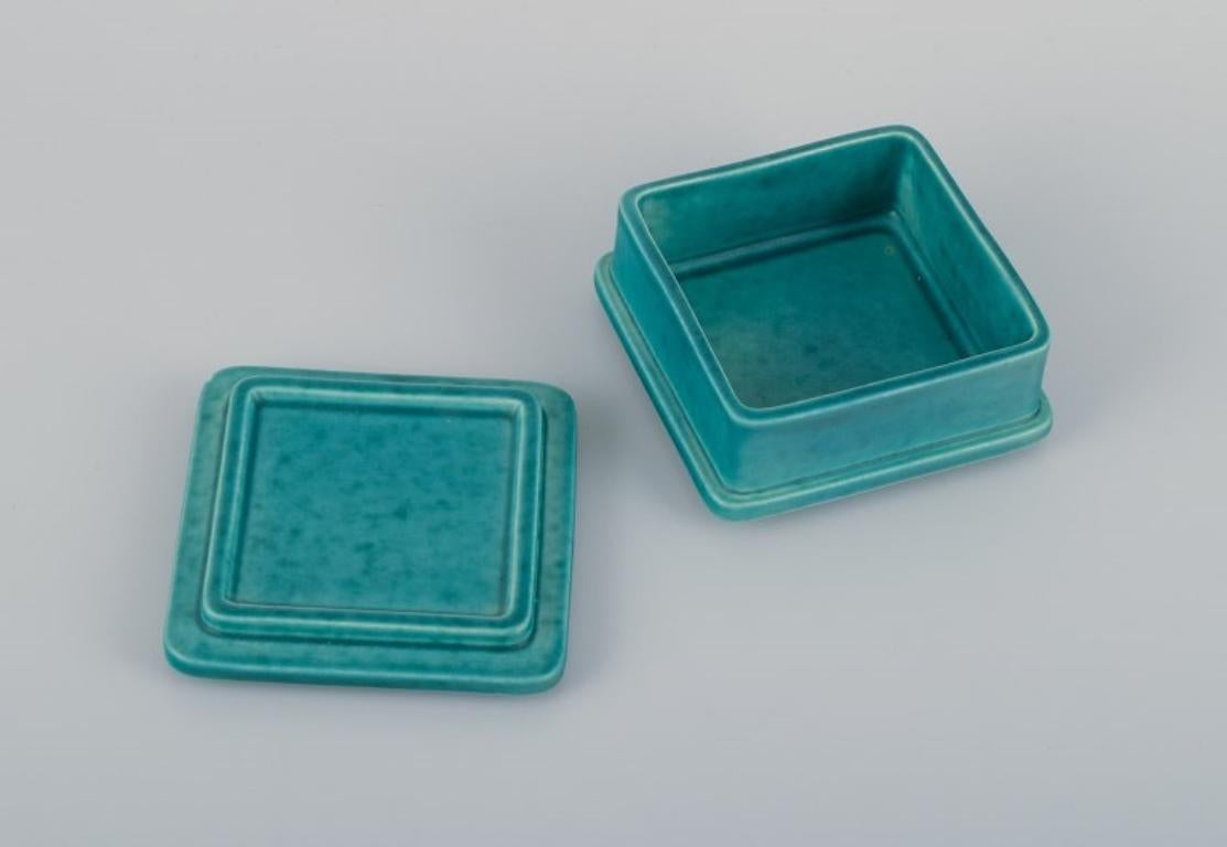 Wilhelm Kåge (1889-1960) for Gustavsberg, Sweden. 
Square Art Deco lidded box in ceramic with classic green glaze. 
From the Argenta series.
Mid-20th century.
Marked.
In perfect condition.
Dimensions: D 10.0 cm x H 5.5 cm.

Wilhelm Kåge is a