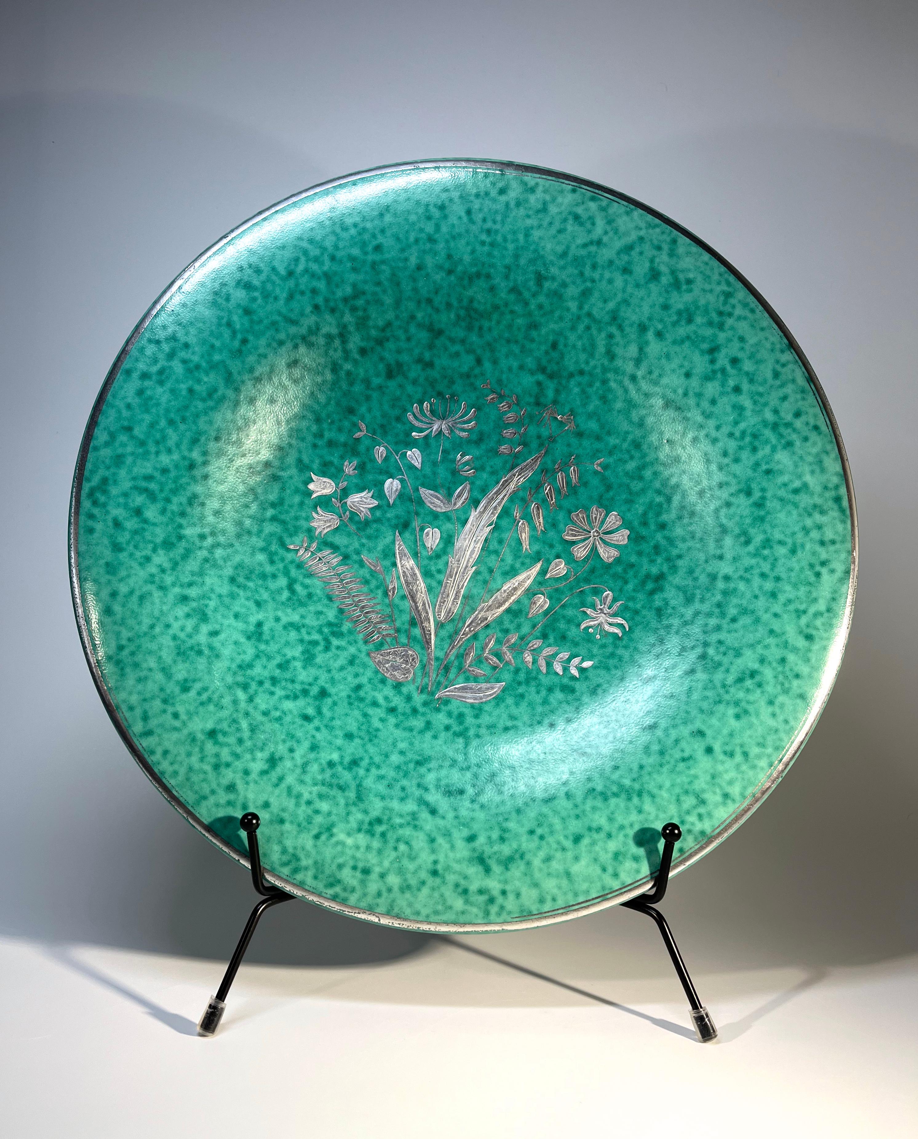 Floral round stoneware centrepiece Argenta platter by Wilhelm Kage for Gustavsberg
Applied silver floral central decoration of spring flowers and foliage. 
Interesting folly: Kage has placed a long legged spider atop the foliage
The outer rim has a