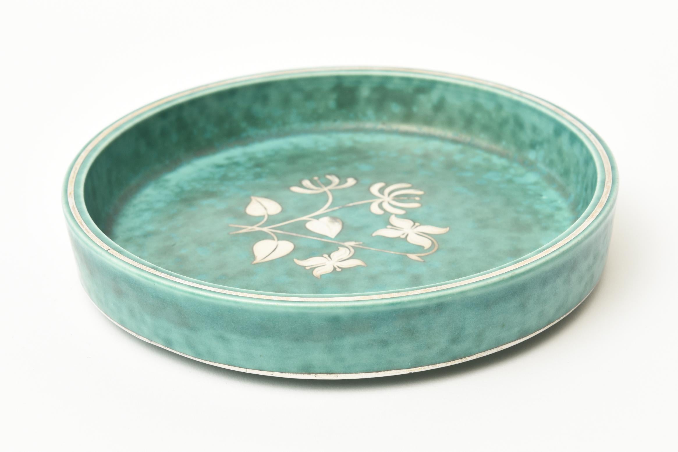 This lovely vintage Swedish Gustavsberg Argenta ceramic bowl or low dish has inlaid sterling silver overlay of formations of nature. Flower and leave depictions form the interior of the bowl. The infamous color of these ceramics are a turquoise
