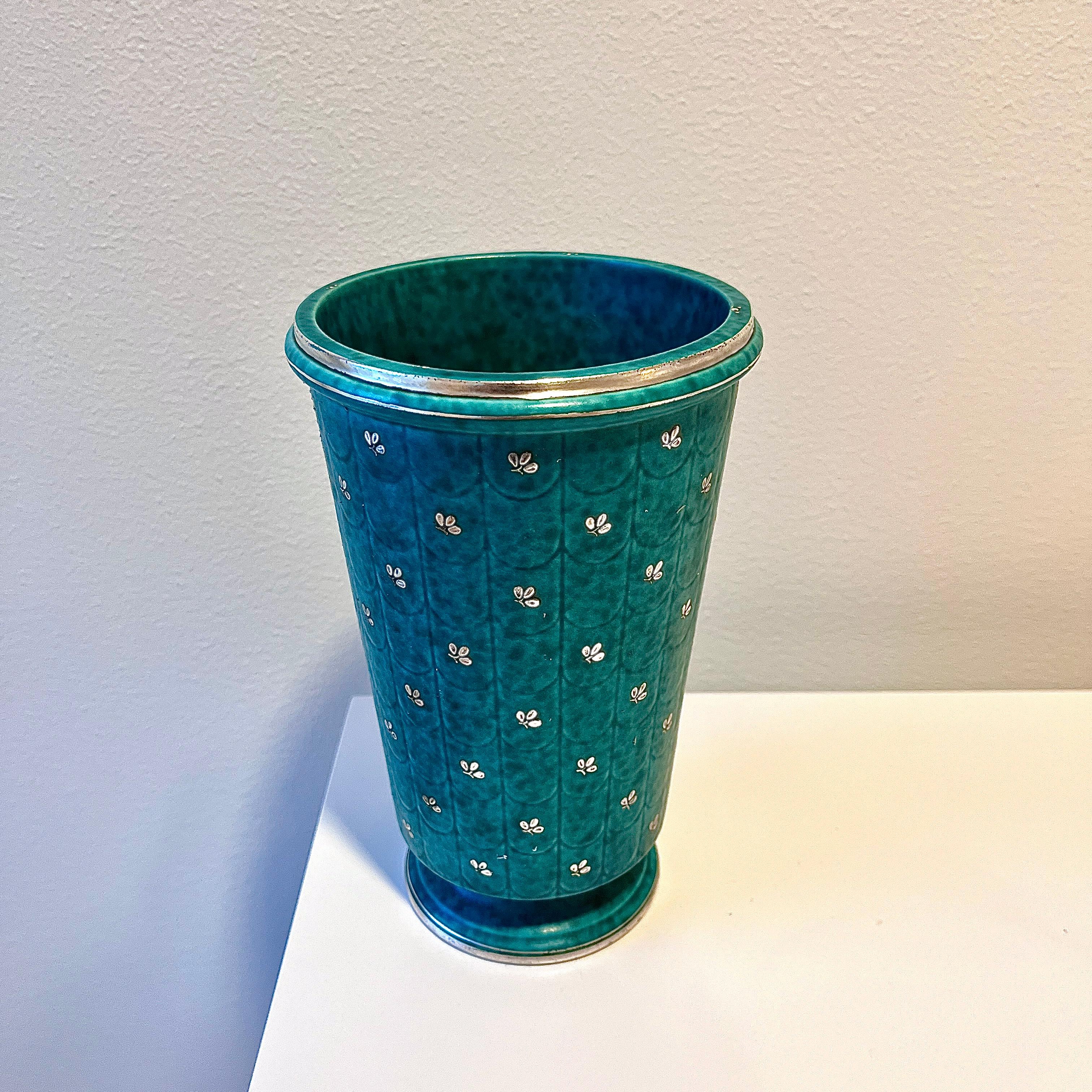 Stoneware vase designed by Wilhelm Kåge from the ‘Argenta’ series for Gustavsberg, Sweden, 1931. Signature green glaze with decor of flowers and stripes at the rim and base in silver.

Signed in silver at the base.

In great condition, smaller signs