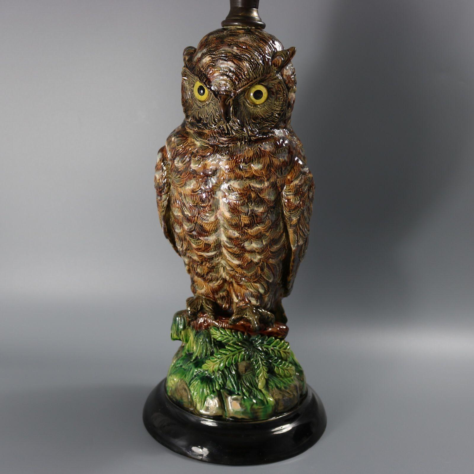 Base y quemador de lámpara de mayólica Schiller que presenta un búho posado en una rama sobre rocas y follaje. El búho tiene ojos de cristal originales. Coloración: predominan el marrón, el verde y el gris. La pieza lleva marcas de fabricante de la