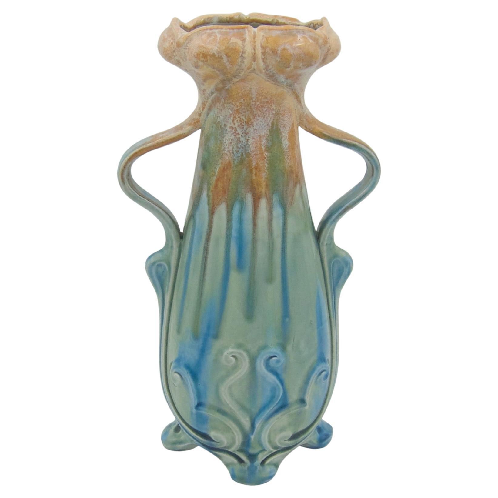 A tall art pottery vase by Wilhelm Schiller and Son (WS&S) of Bohemian, dating circa 1900.  The Art Nouveau vase rests on four splayed feet and is decorated with scroll motifs in relief and sinewy lines trailing up the sides of the body toward