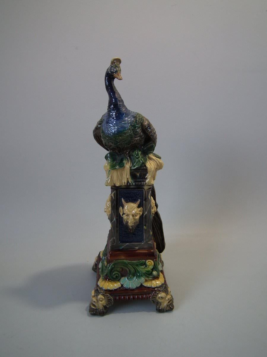 Schiller Majolica vase which features a peacock seated on a pedestal. Coloration: Blue, green, yellow, are predominant. The piece bears maker's marks for the Schiller pottery. Bears a pattern number, '384'.