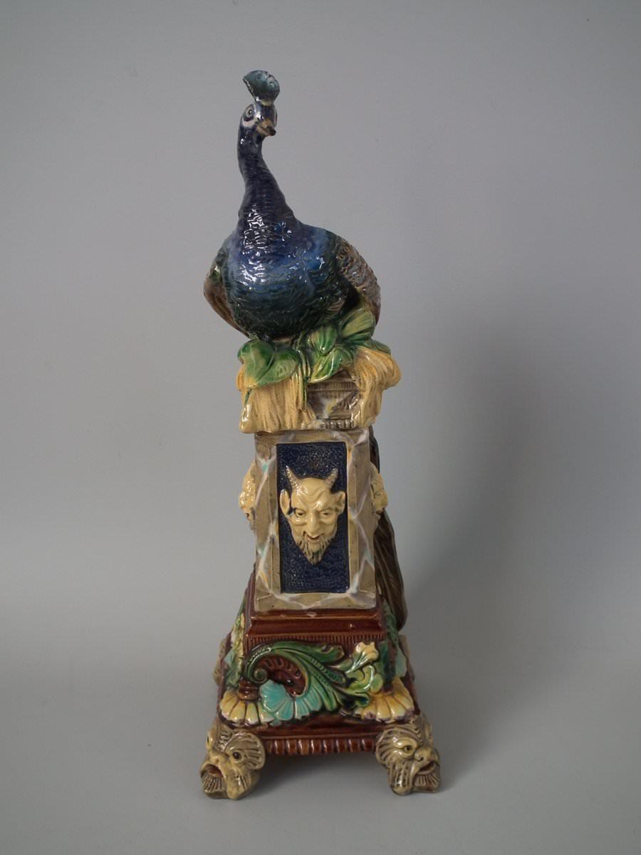 Schiller Majolica vase which features a peacock seated on a pedestal. Coloration: blue, green, yellow, are predominant. The piece bears maker's marks for the Schiller pottery. Bears a pattern number, '384'.