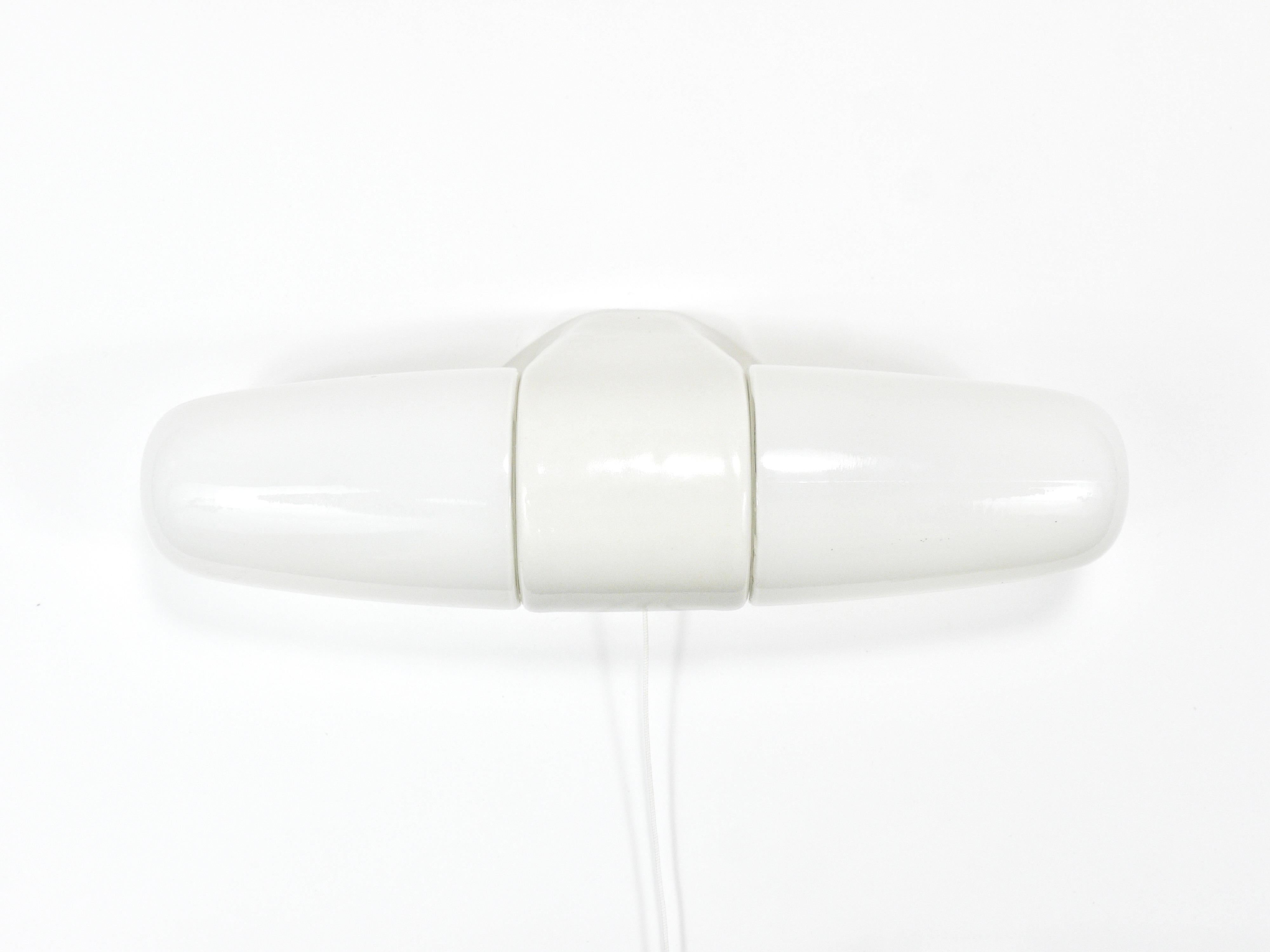 Aplique/plafón de pared de doble casquillo de la Modernidad de mediados de siglo, de la década de 1950, diseñado por Wilhelm Wagenfeld. Su forma se asemeja a la de un zepelín o un puro, fabricado en porcelana con esmalte blanco y rematado con dos