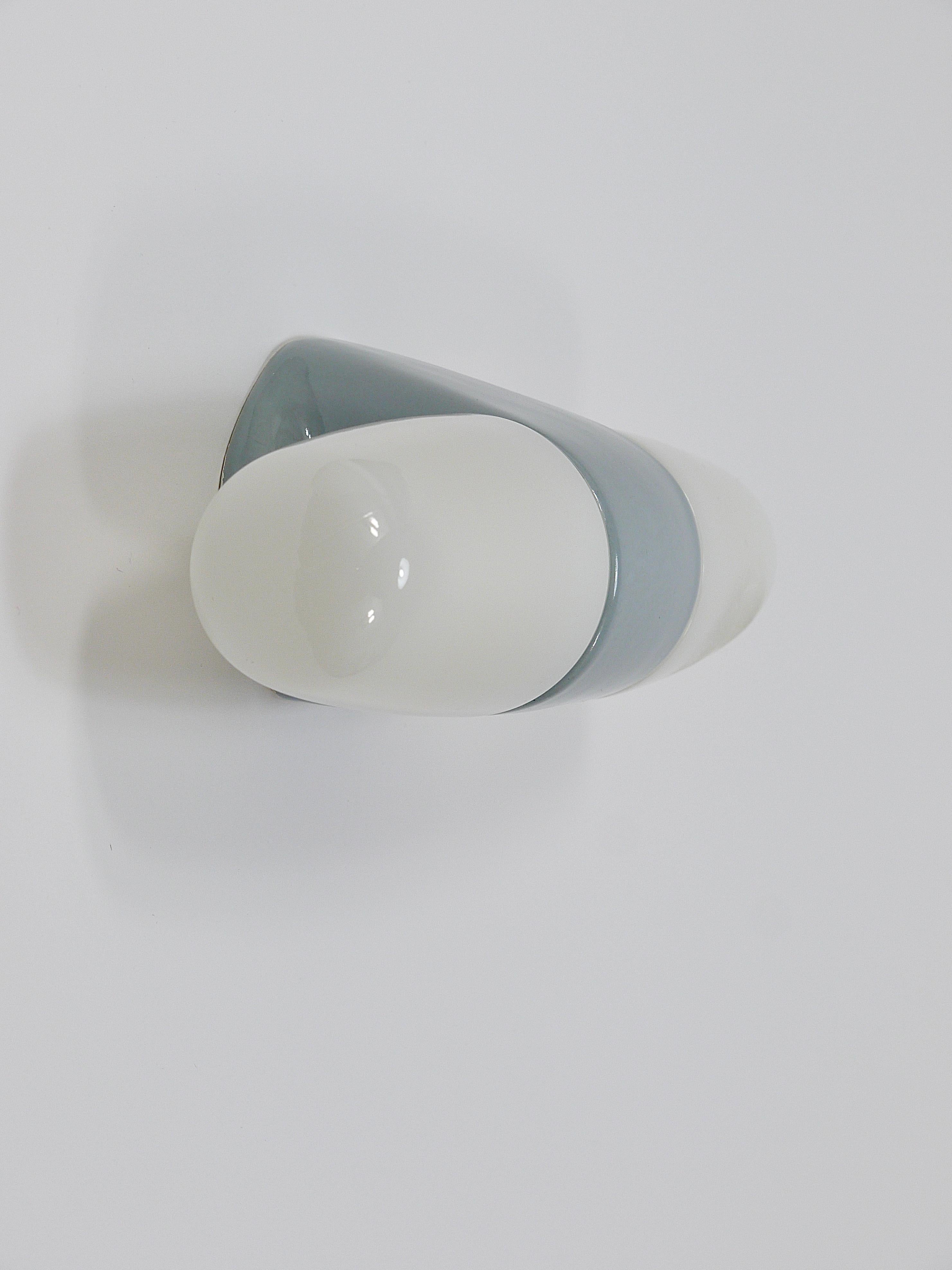 Lampe murale/applique à double prise datant des années 1950, conçue par Wilhelm Wagenfeld. En porcelaine avec une glaçure grise brillante accentuée par deux abat-jour/couvercles d'ampoules en verre opalin blanc. D'après notre expérience, la version