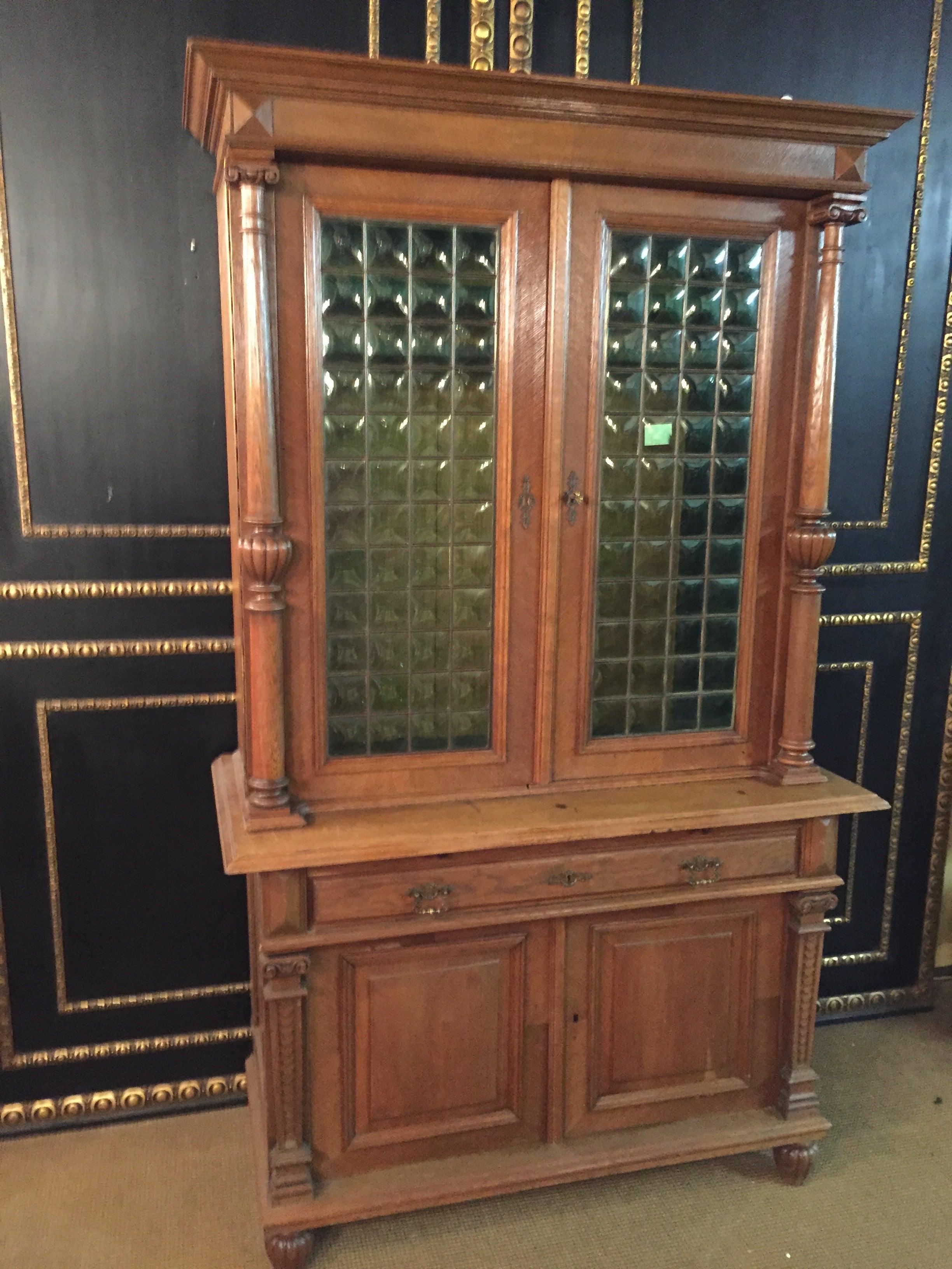Massive oak manufactured circa 1900 impresses among other things by its carved front, the great green glasses, one glass pane is unfortunately broken
right and left columns.


The cabinet is in good original condition with age-related signs of