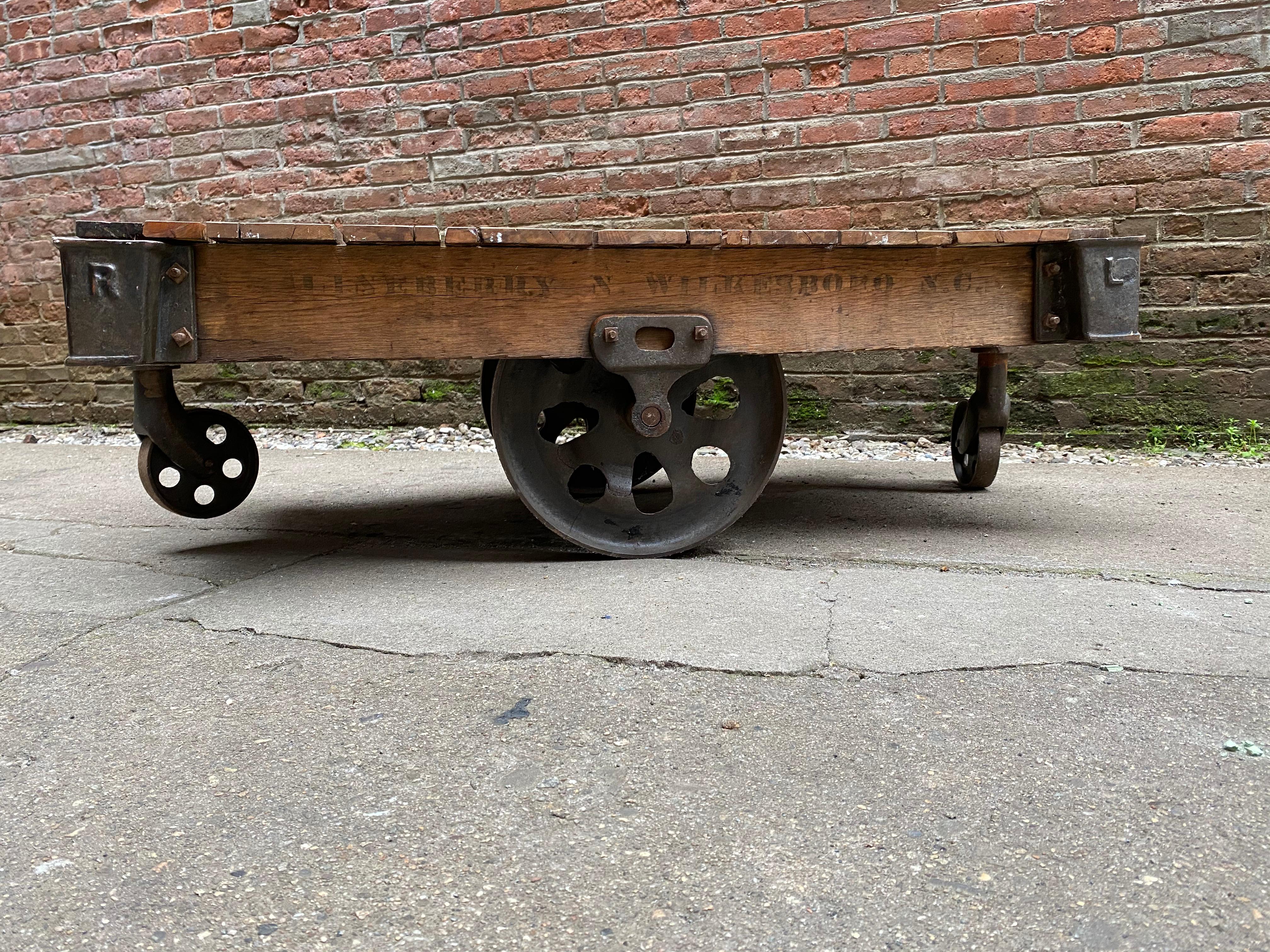 Early industrial iron with wood slat rolling cart. Heavy duty cast iron wheels. Stencil graphics on the side of the cart, N. Wilkesboro, NC. It looks as if the wood platform has been refinish or cleaned up. Rolls nicely. 

Structurally sound and