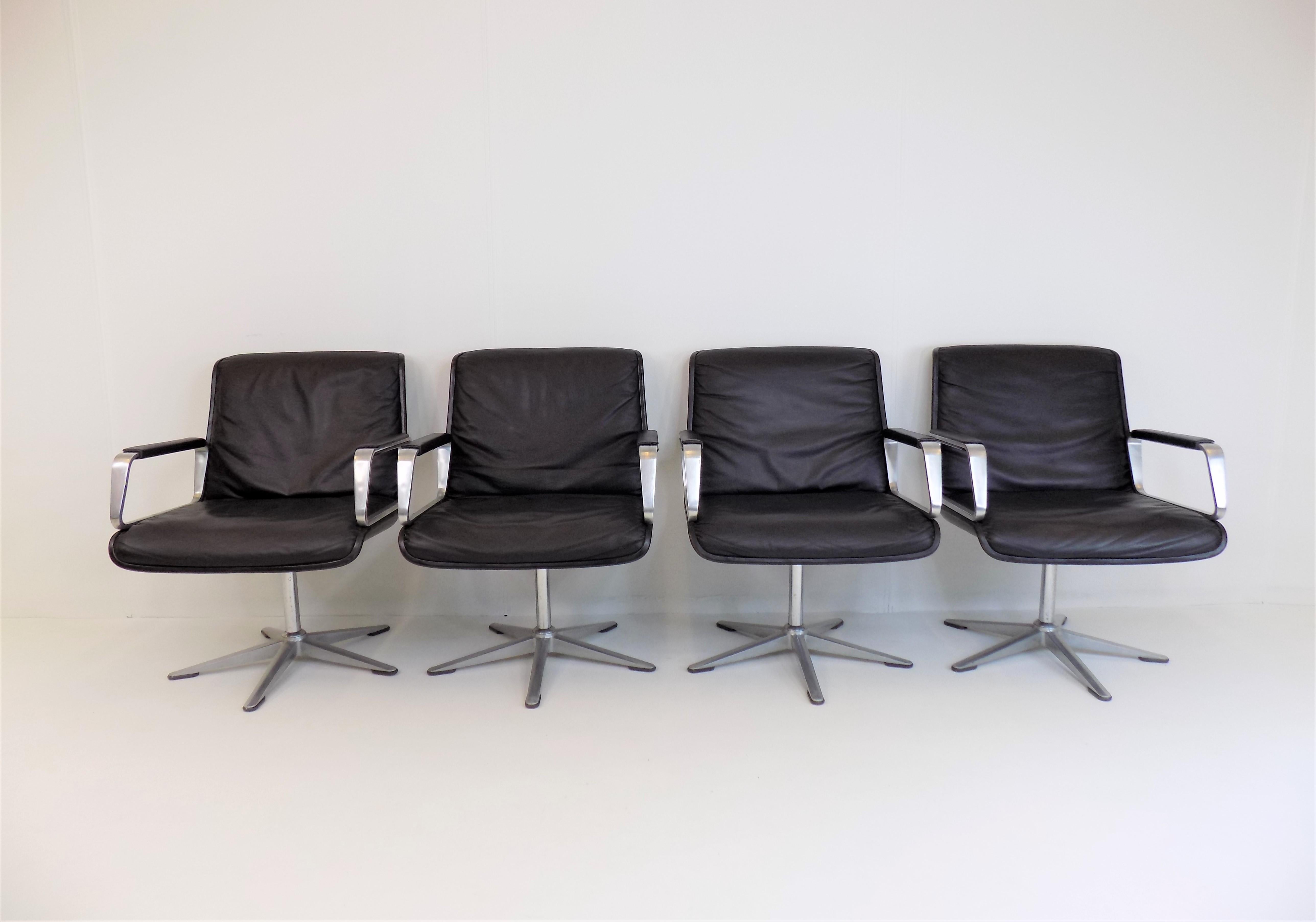 This set of 4 Wilkhahn Delta leather armchairs of the early generation, with brushed aluminum armrests with leather pads and with black shells, is in excellent condition. The leather is flawless, the plastic shells and the aluminum feet only have