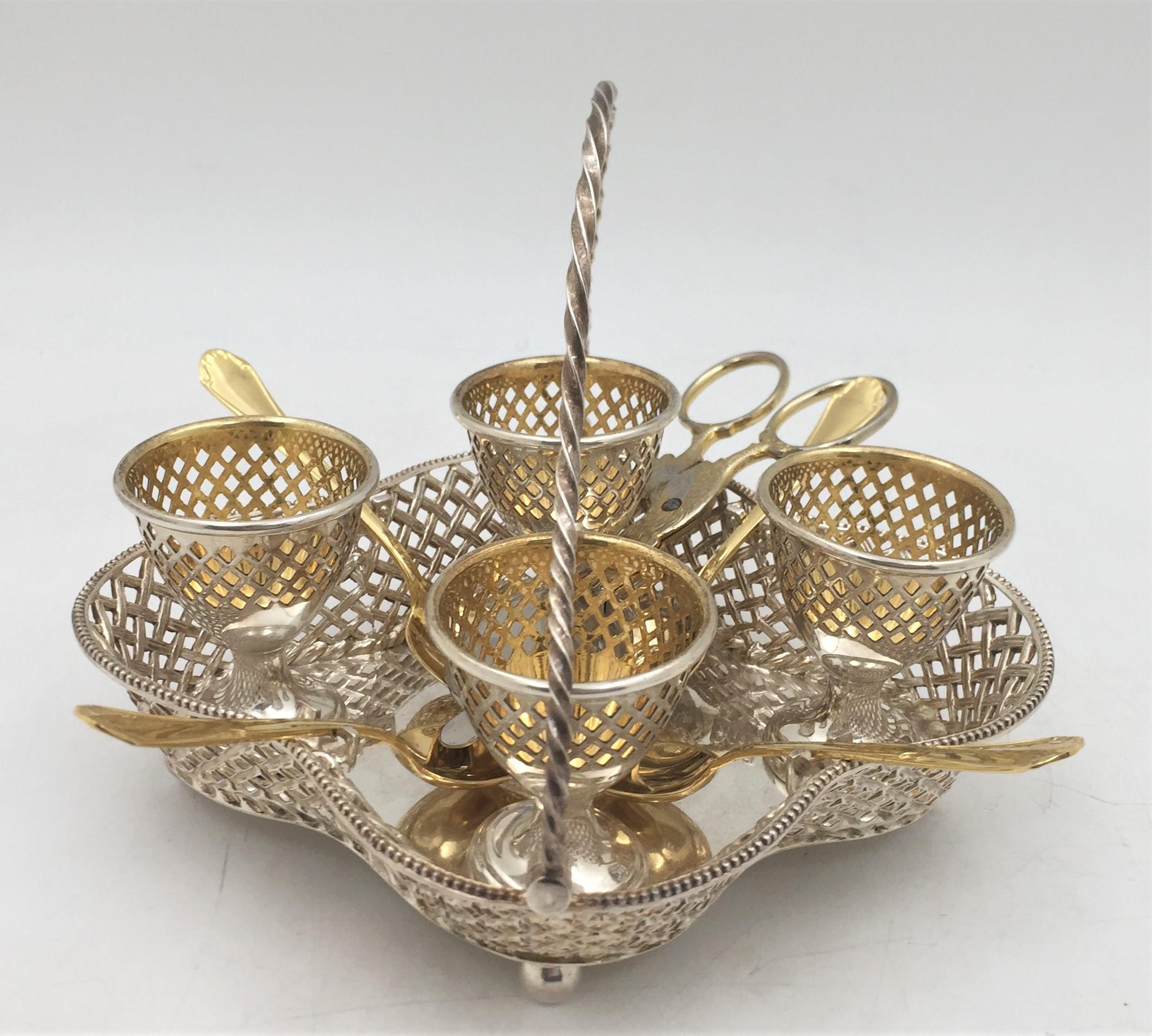 Wilkinson & Co., sterling silver egg coddler stand holder in Victorian style from 1880 with 4 sterling silver egg holders. It is accompanied by 4 gilt sterling silver spoons and an egg server that exhibits a refined chicken motif. The pierced egg