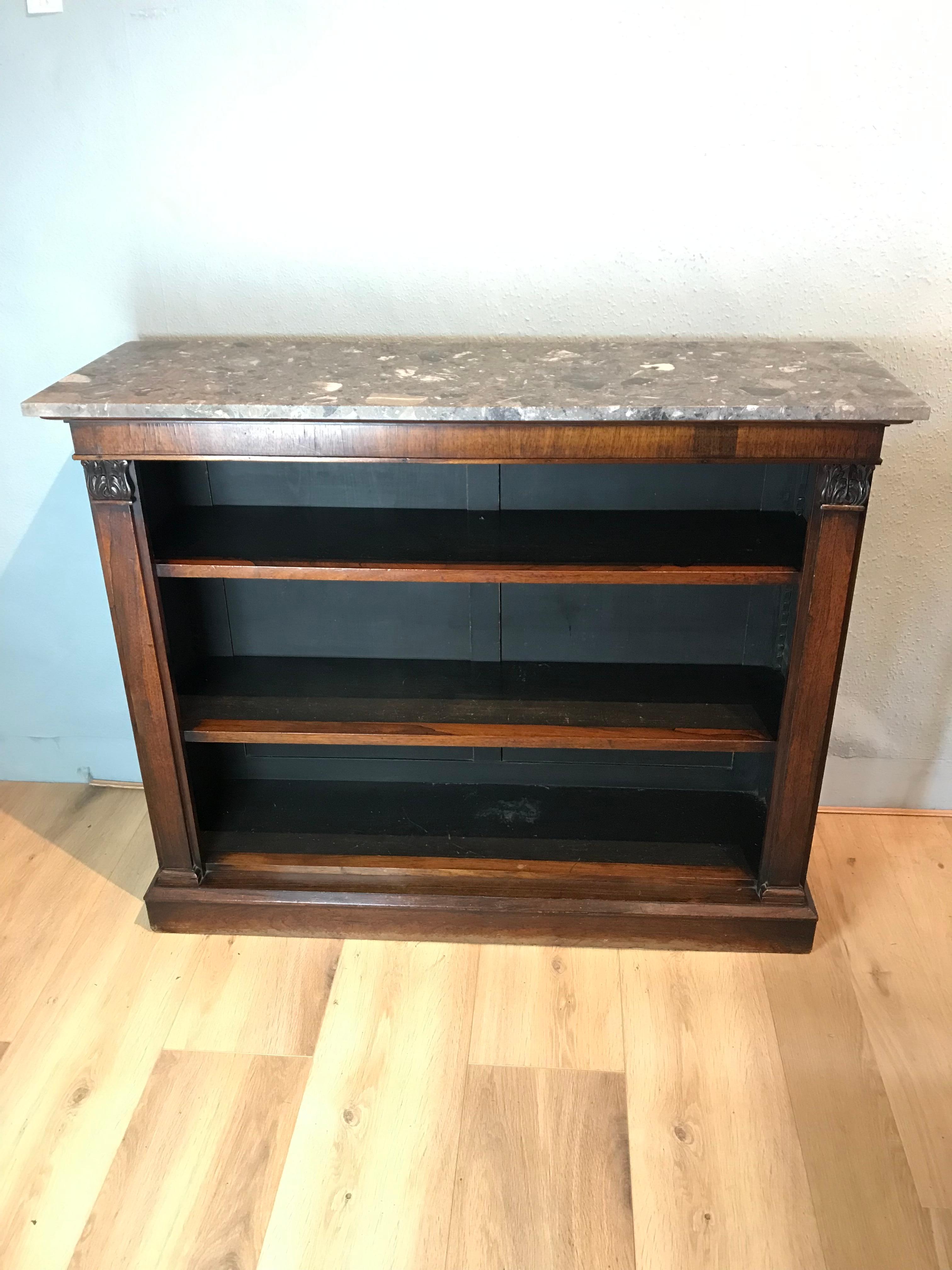 A free standing marble topped William 4th rosewood bookcase. The bookcase consists of two adjustable shelves, flanked by two pillars with carved leaf capitals, resting on a plinth base. This attractive bookcase retains its original patina with