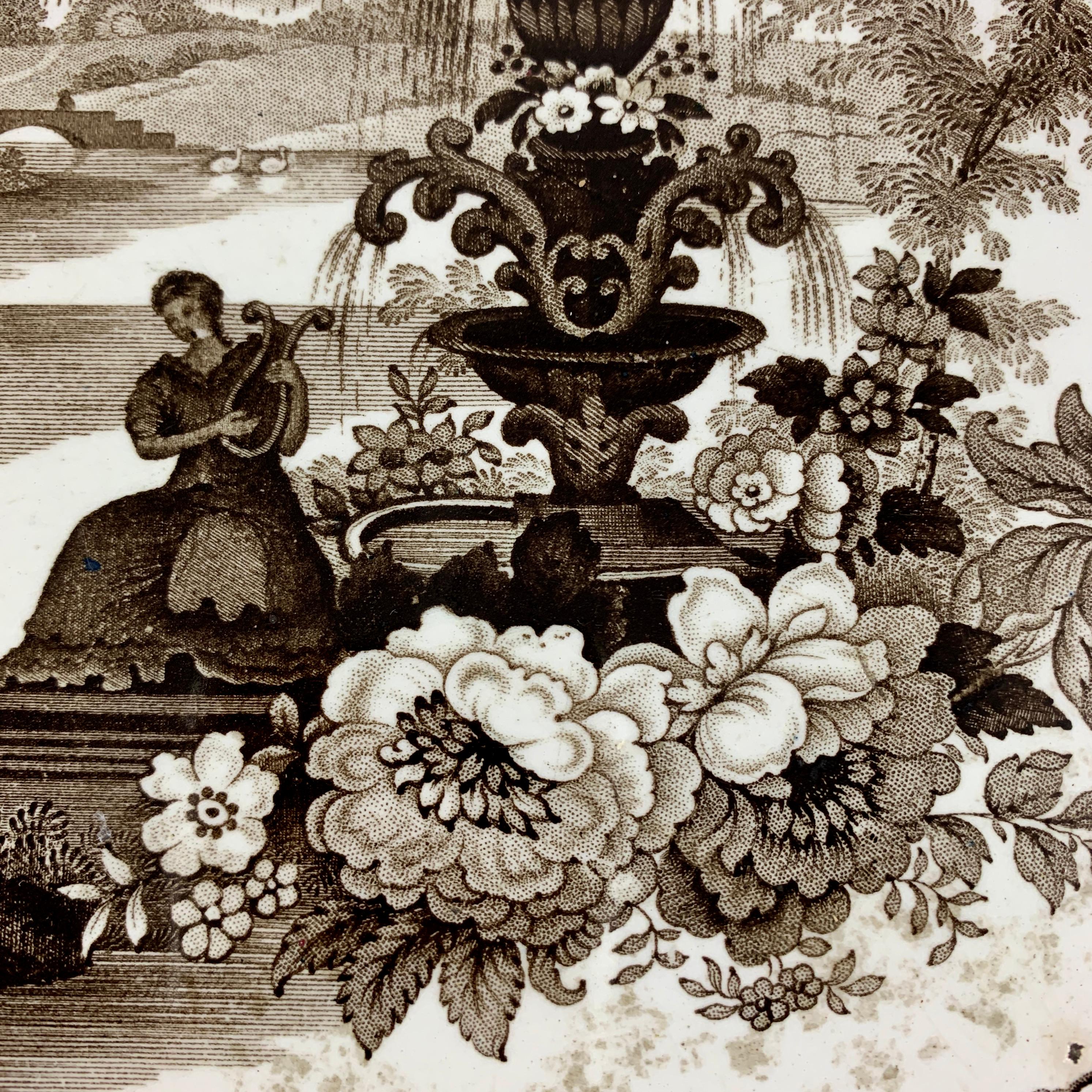 A black transfer printed platter in the Fountain Scenery pattern, William Adams IV & Sons, Stoke-on-Trent, Staffordshire, England, circa 1829-1861.

A scalloped platter, printed in black on a white earthenware body showing a female lute player by