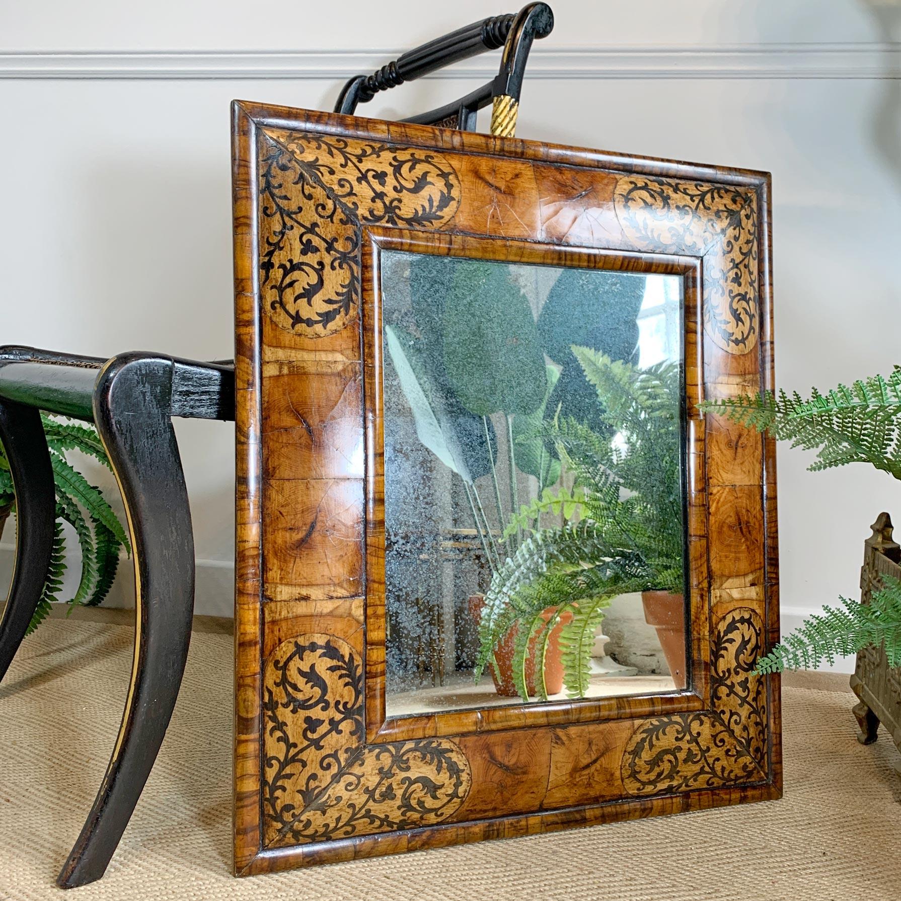 An outstandingly beautiful William and Mary walnut cushion mirror, the deep cushion frame decorated with scrolling flora and fleur de lis marquetry veneer. The frame is complete, with no losses and we believe the foxed mirror plate to be original.