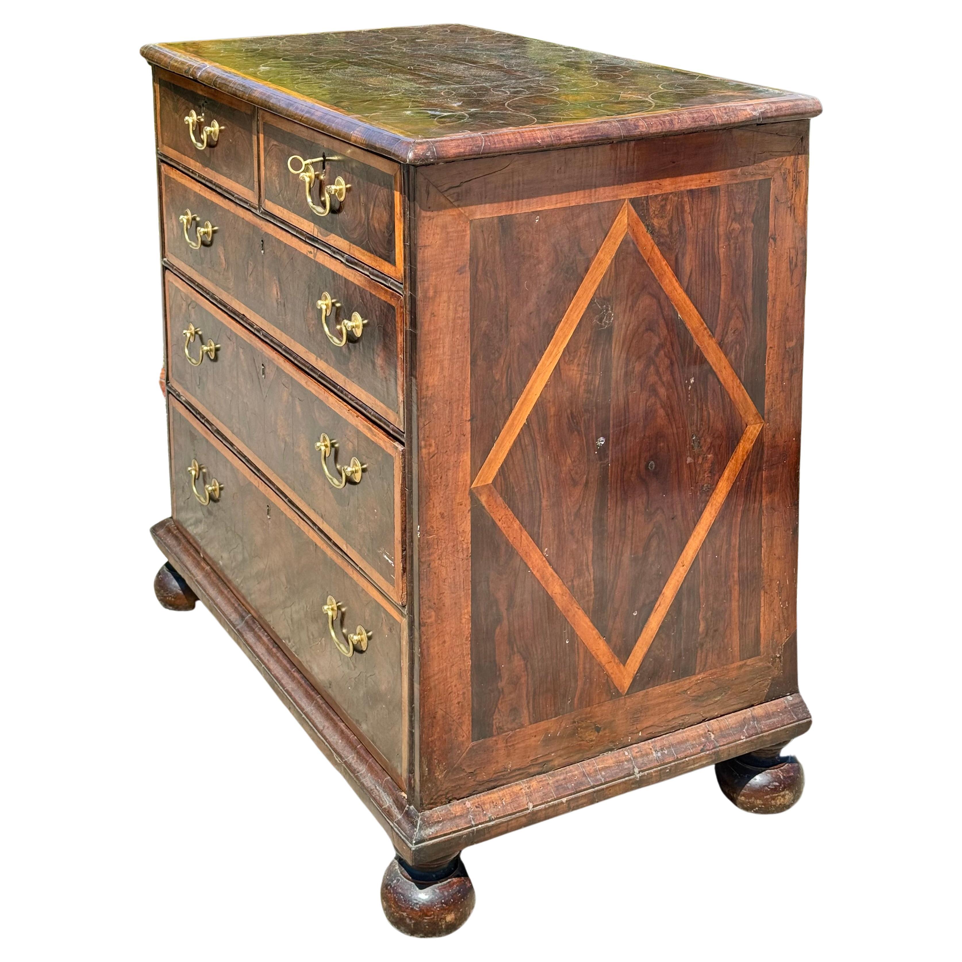 Cassettiera in noce impiallacciata in radica di William & Mary del XVIII secolo. La cassettiera presenta due cassetti corti su tre cassetti lunghi graduati, cassetti a coda di rondine con ferramenta in ottone. La cassapanca poggia su piedini a