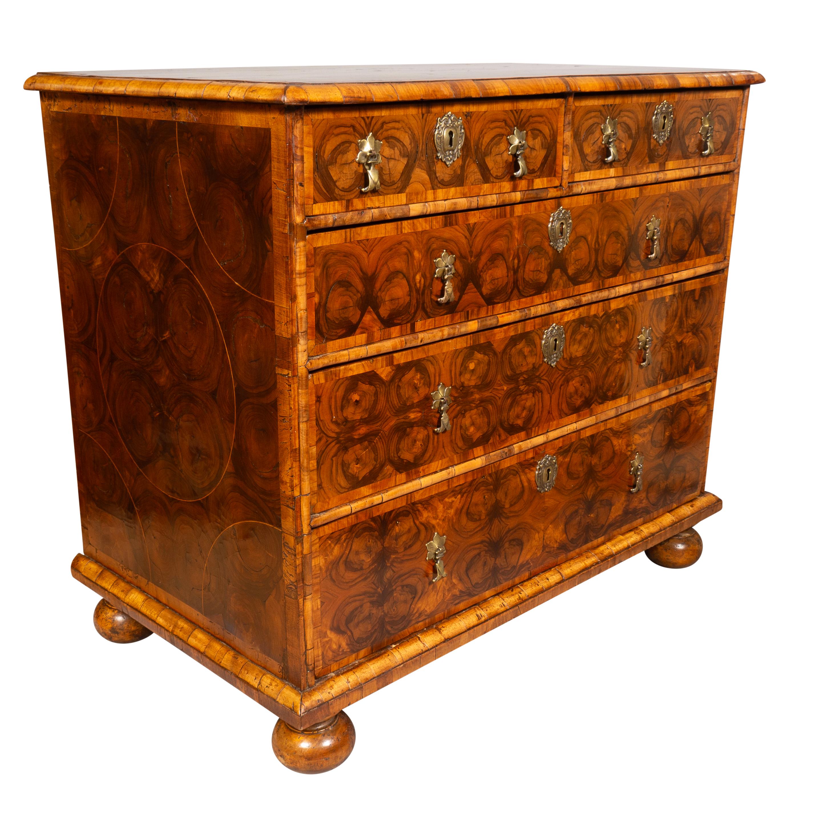 With a rectangular top with rounded edge and a top inlaid with rings of cross cut branch veneers forming a pattern of rings. The conforming case with repeating oyster decoration with two over three drawers with brass tear drop handles. Sides with