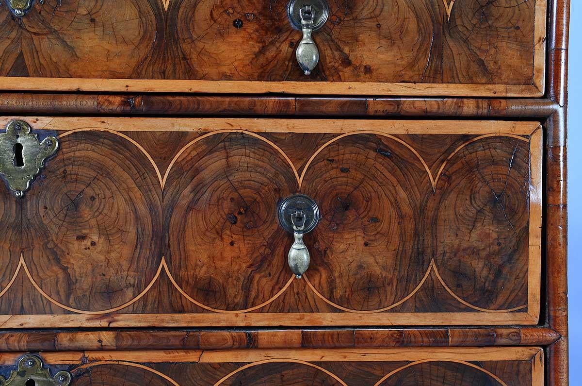 Una cassettiera impiallacciata in noce ostrica del periodo William & Mary su piedi a castello. La configurazione dei cassetti è insolita, con quattro cassetti lunghi rispetto ai tipici due corti e tre lunghi. I cassetti, il piano e i lati sono tutti