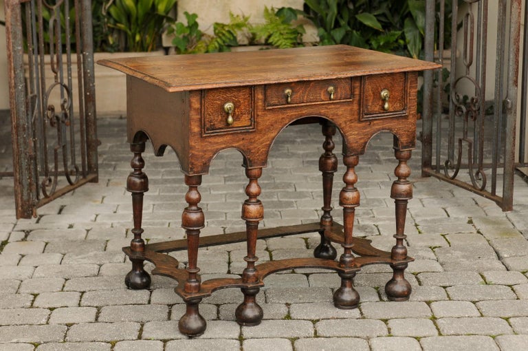 An English William and Mary style oak side table from the early 19th century, with three drawers, trumpet legs and curving side stretcher. Born in the very early years of the 19th century, this exquisite side table presents all the stylistic
