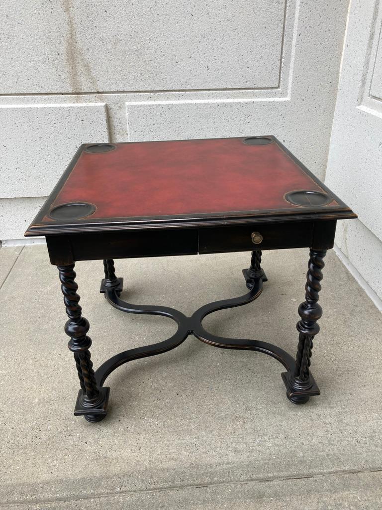 A very handsome ebonized wood card or games table in the English 17th century William and Mary style with barley-twist legs joined by a deeply curved stretcher, supported by ball feet. The red leather top with a tooled gilt border. With four drawers