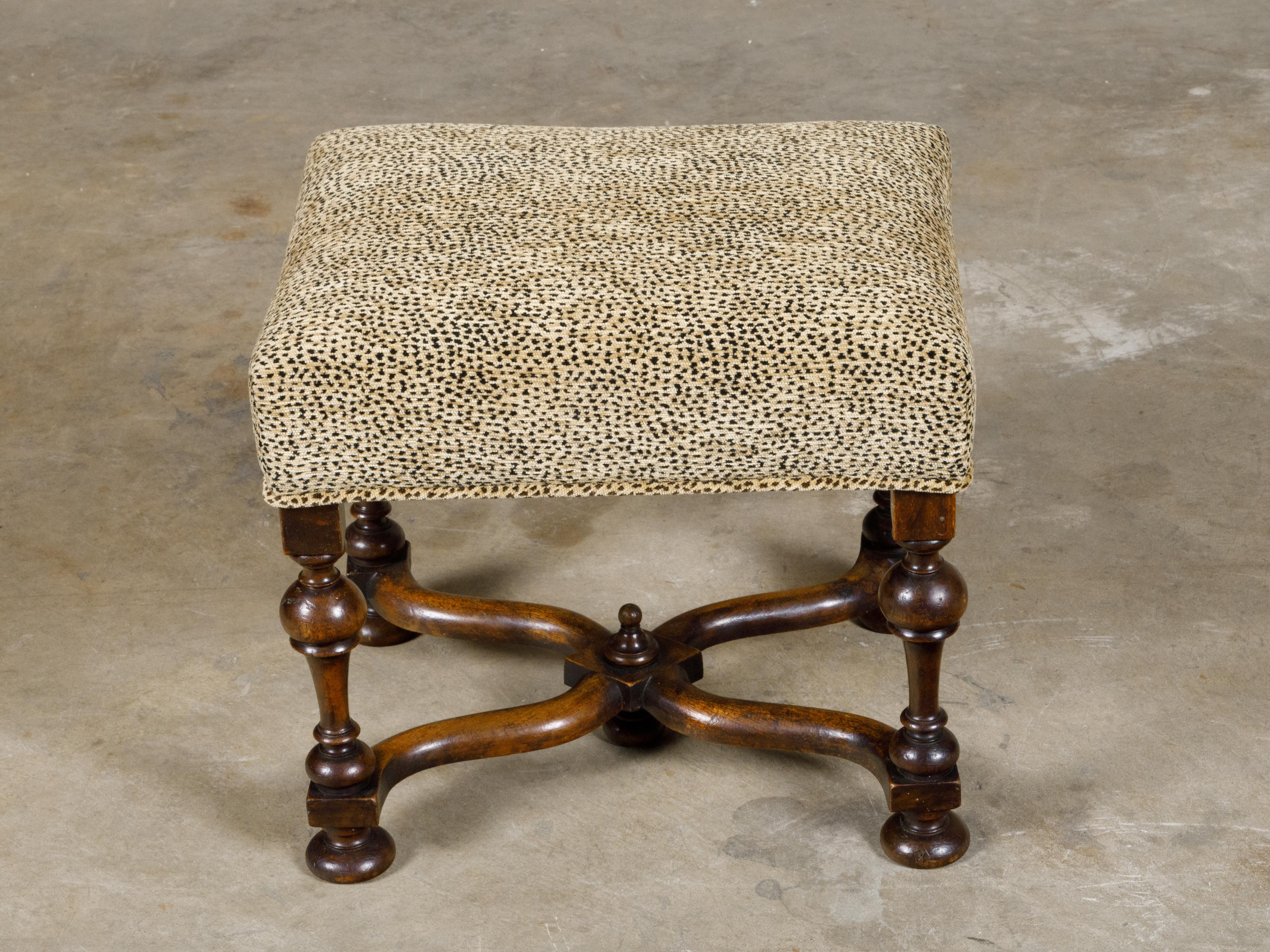 An English William and Mary style stool from circa 1900 with turned legs, curving X-Form stretcher, bun feet and upholstery. This stool, with its turned legs, curving X-Form stretcher with a central finial, bun feet, and plush upholstery, is a
