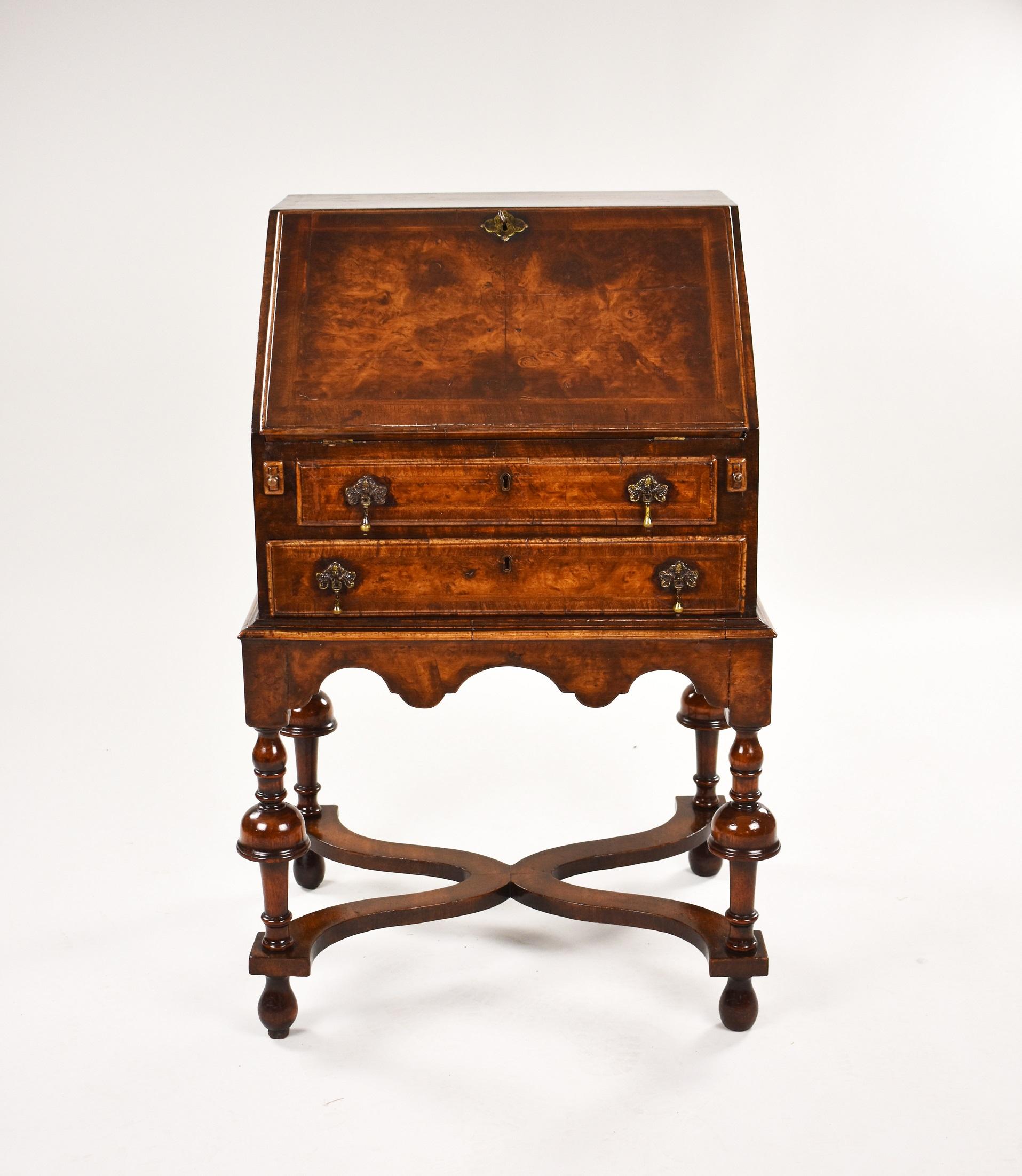 William and Mary style walnut and feather banded bureau on stand. The fall enclosing fitted interior above two drawers on stand with shaped apron and turned legs united by cross stretcher on bun feet.