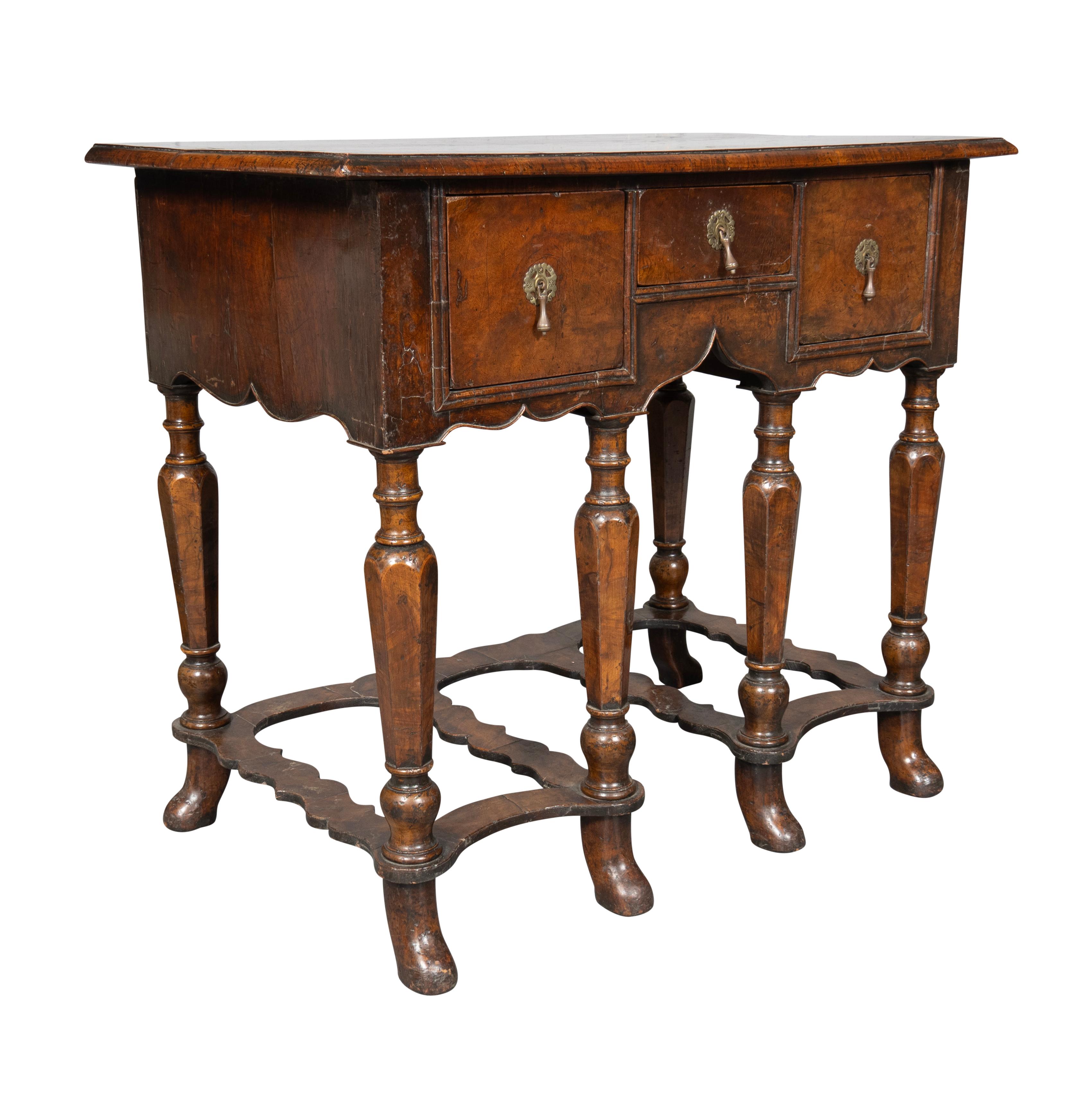 Plateau rectangulaire en ronce de noyer à bord mouluré et bagué. Avec un petit tiroir central et des tiroirs plus grands flanqués, tous avec des poignées en laiton. Elle repose sur des pieds tournés et fuselés, avec des brancards inférieurs.