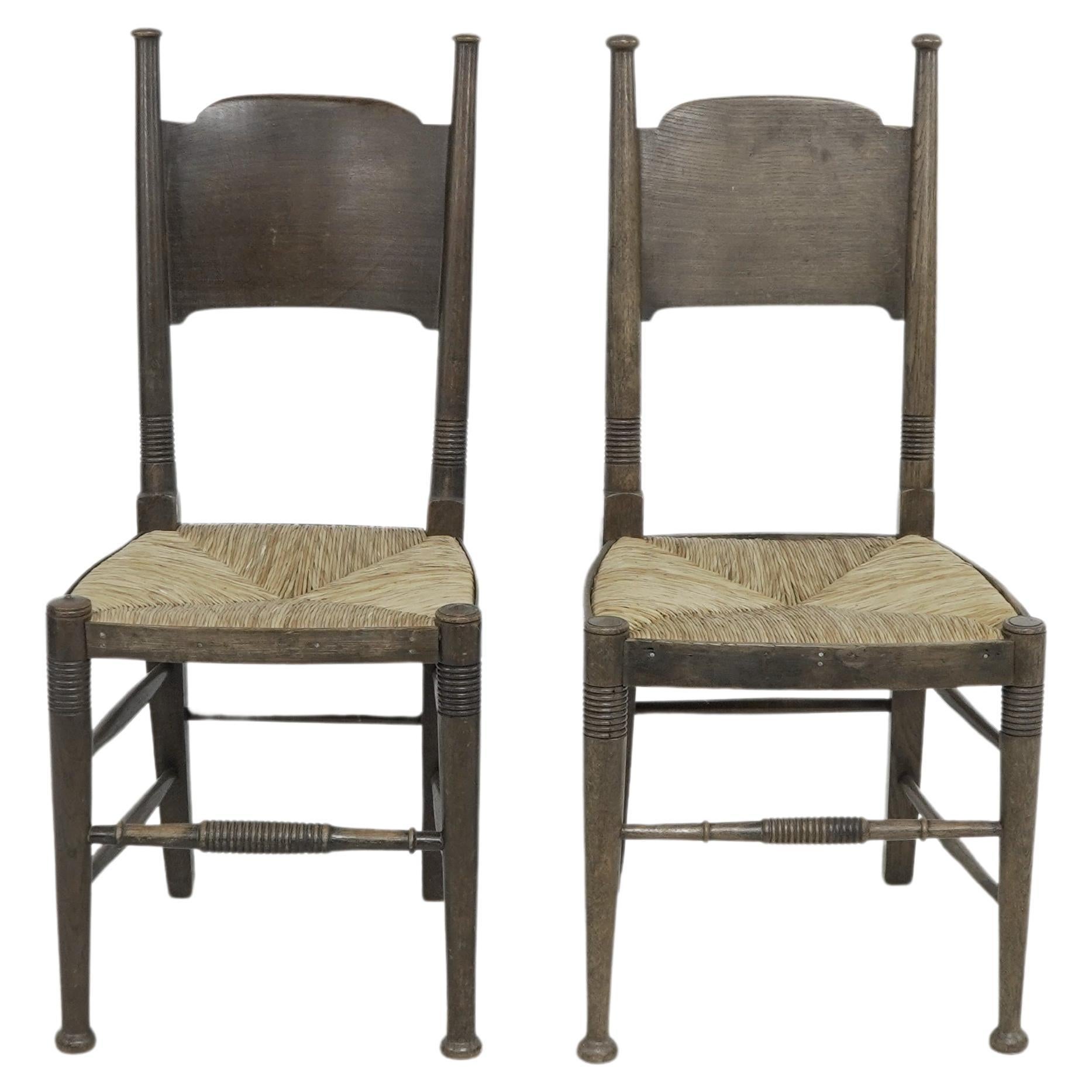 William Birch of High Wycombe. Liberty & Co retailer. 
A pair of Arts & Crafts rush seat oak dining or side chairs with a wide curved headrest and ring turned legs and front stretchers, retaining the original rush seat side protector strips. 
These