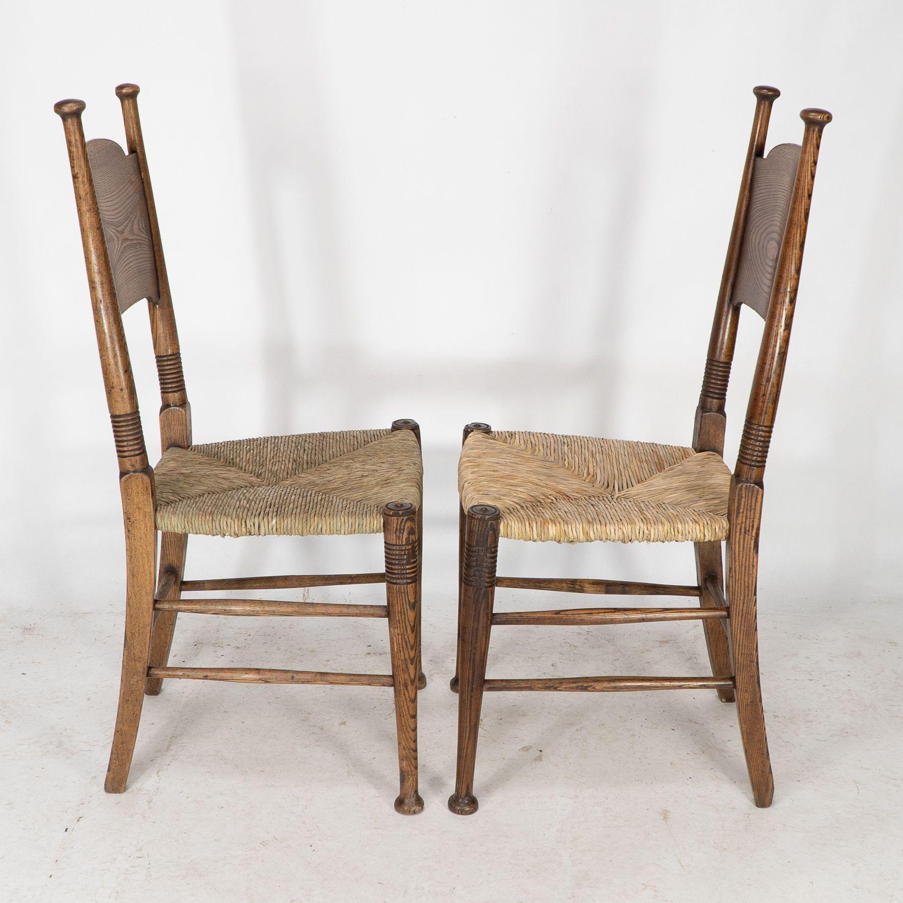 William Birch. Liberty and Co retailer. A classic pair of Arts and Crafts rush seat oak chairs with a wide curved headrest and attractive wild grain. Ring turned legs with ring turned front stretchers. These timeless designs were unique to William