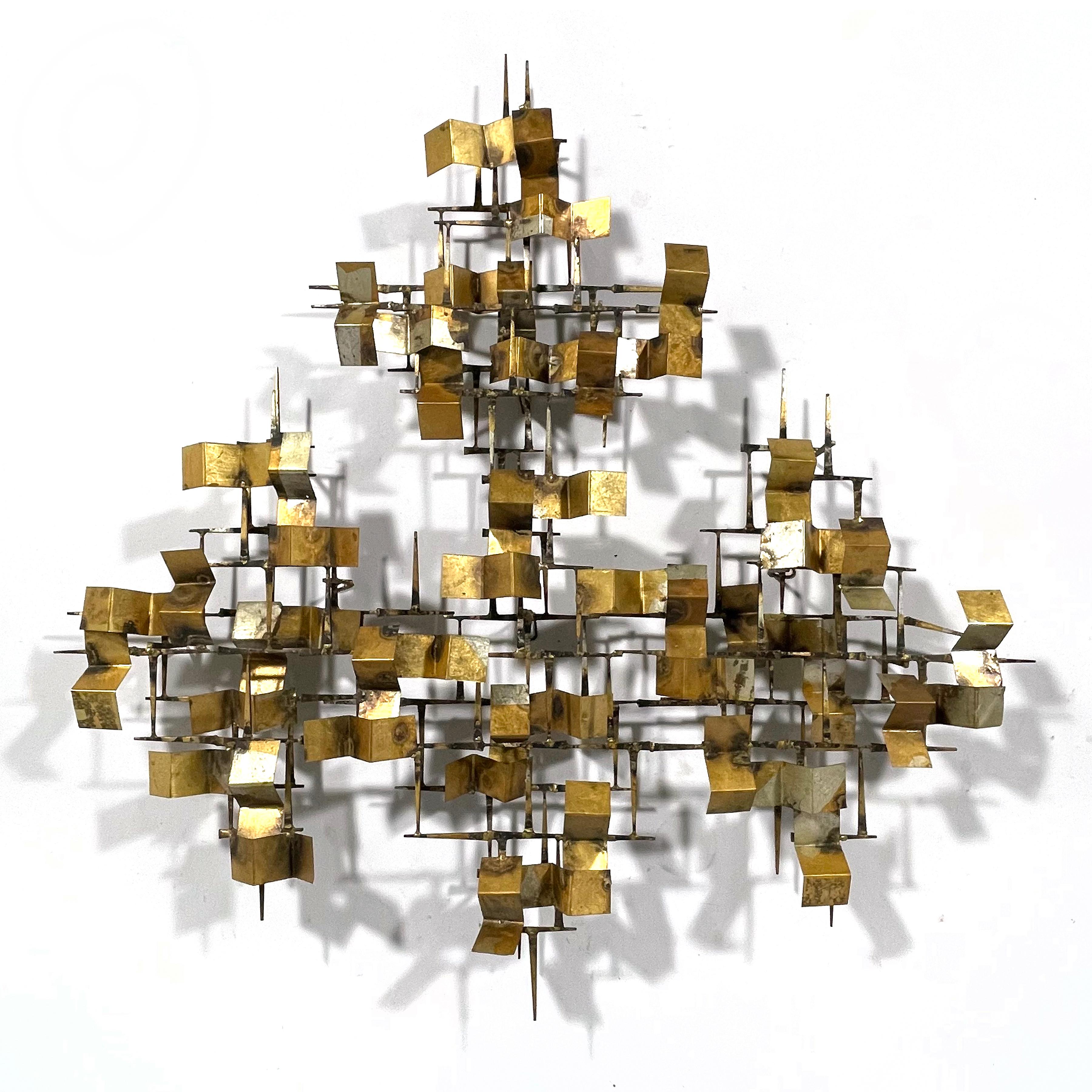 This dynamic abstract wall sculpture by William Bowie is a visual delight and activates any wall it is installed on. A composition of iron brick nails are welded with bronze and overlaid with a series of folded brass forms which have been partially