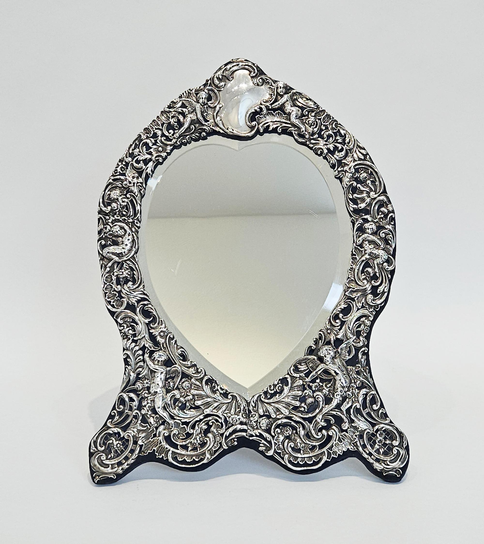 Un elaborato e attraente specchio da toeletta o vanità vittoriano a forma di cuore, realizzato da William Comyns di Londra nel 1906. 

Lo specchio ha un'elaborata faccia in argento massiccio repousé a scorrimento con angeli alati tra arabeschi