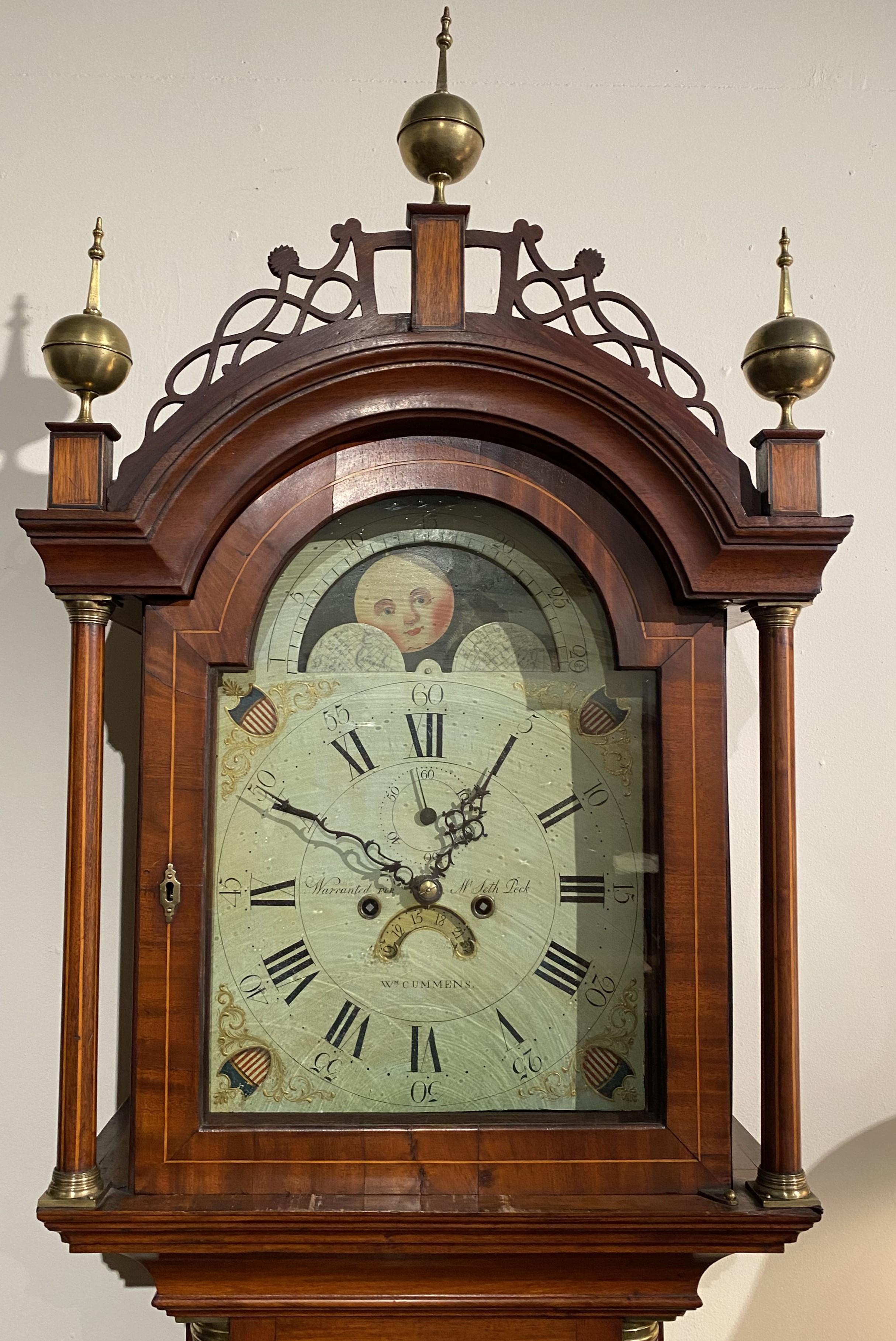 An exceptional Federal mahogany tall case clock with a delicate fretwork crest, adorned with three ball and spire brass finials, surmounting an arched form glass door, opening to a hand painted Roman numeral metal clock face with moon phase,