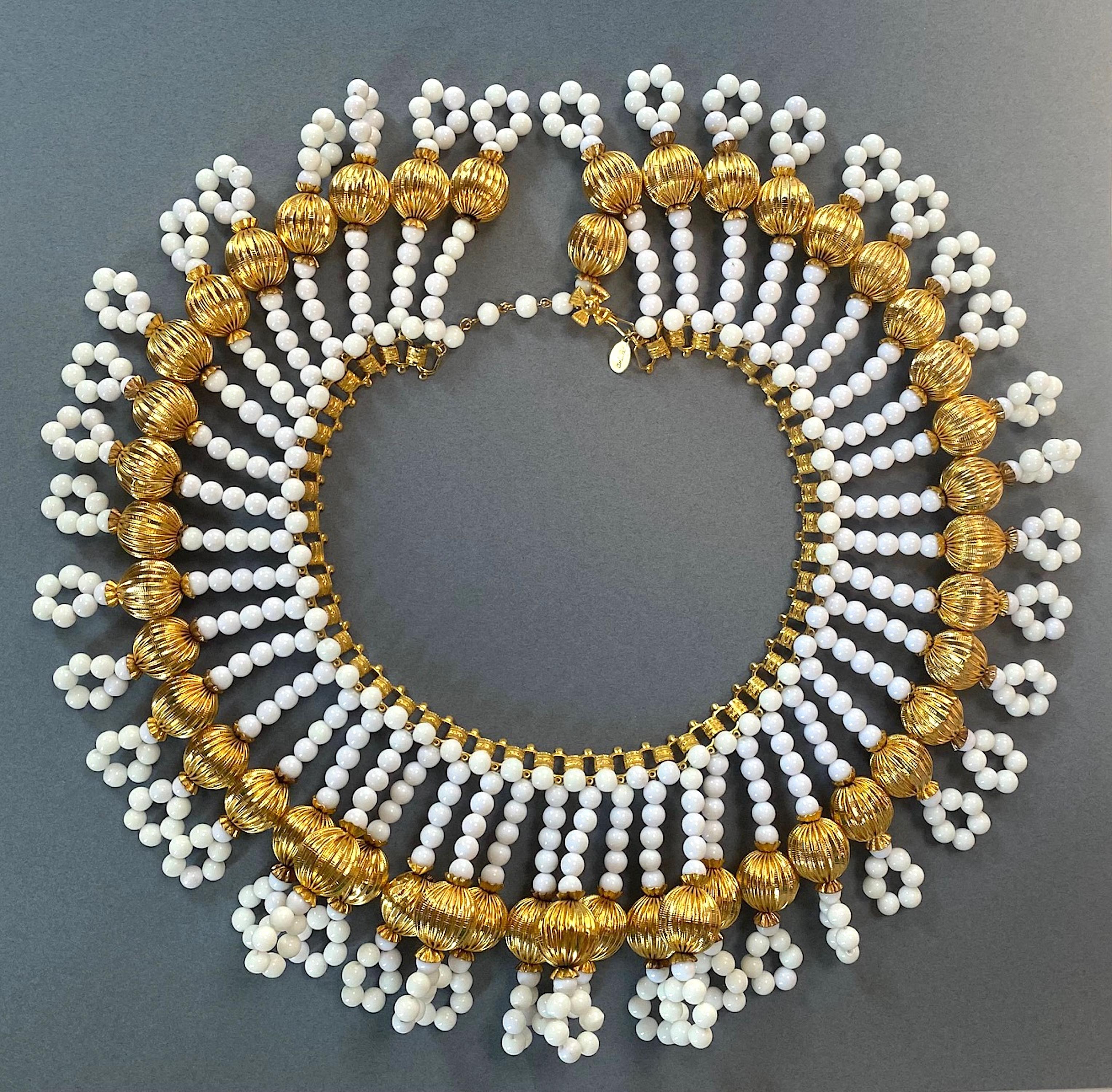 A dramatic large collar necklace by designer William De Lillo from the late 1960s to early 1970s. The necklace is comprised of a gold plate book chain style necklace with 45 hand strung 6 mm white glass bead fringe. Each fringe is accented with a