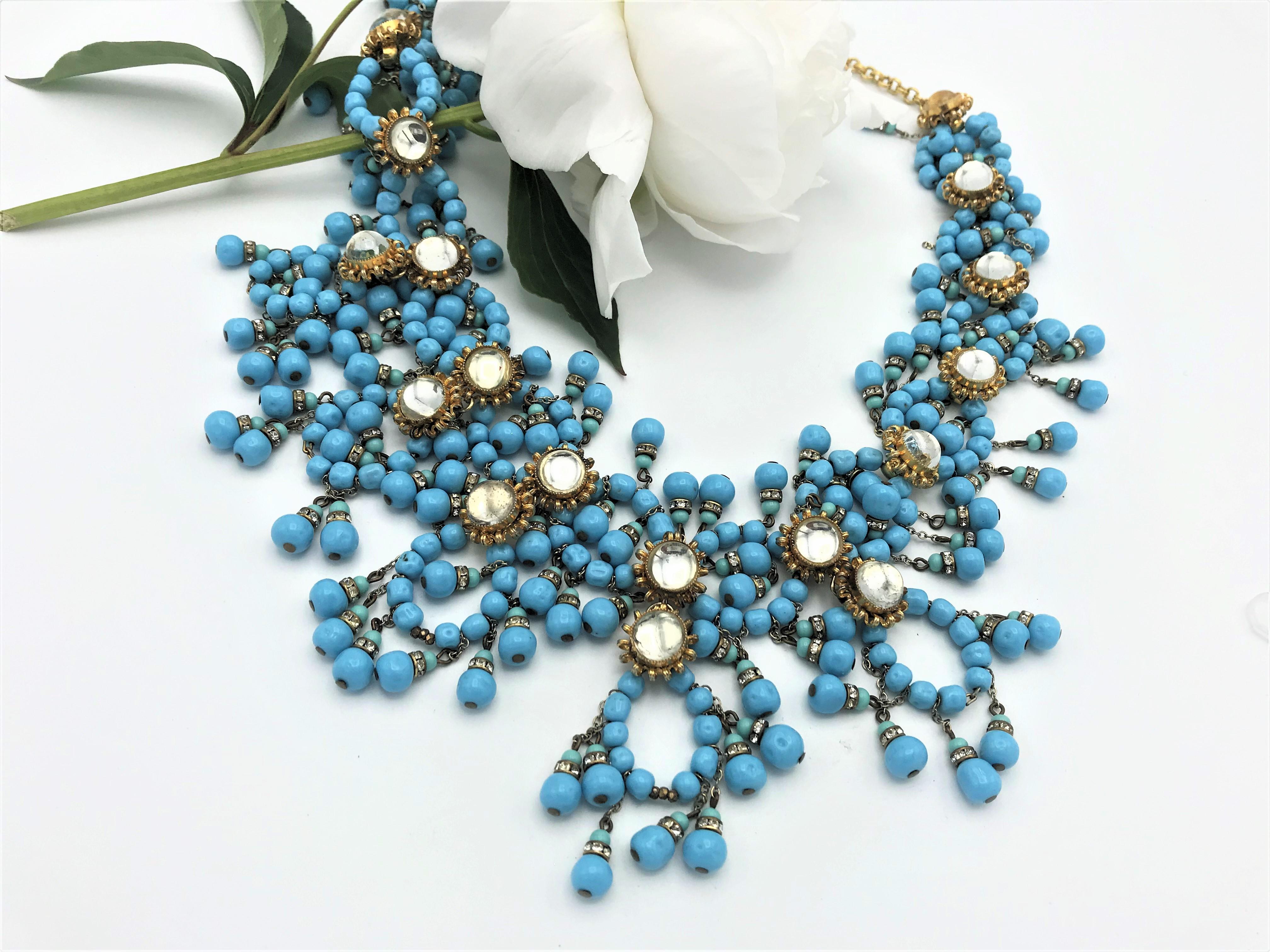 A beautiful imaginative necklace designed by William de Lillo. Consisting of many turquoise colored glass beads, different circles that are hung with many small turquoise tassels, as well as rosettes with round clear rhinestones connect the