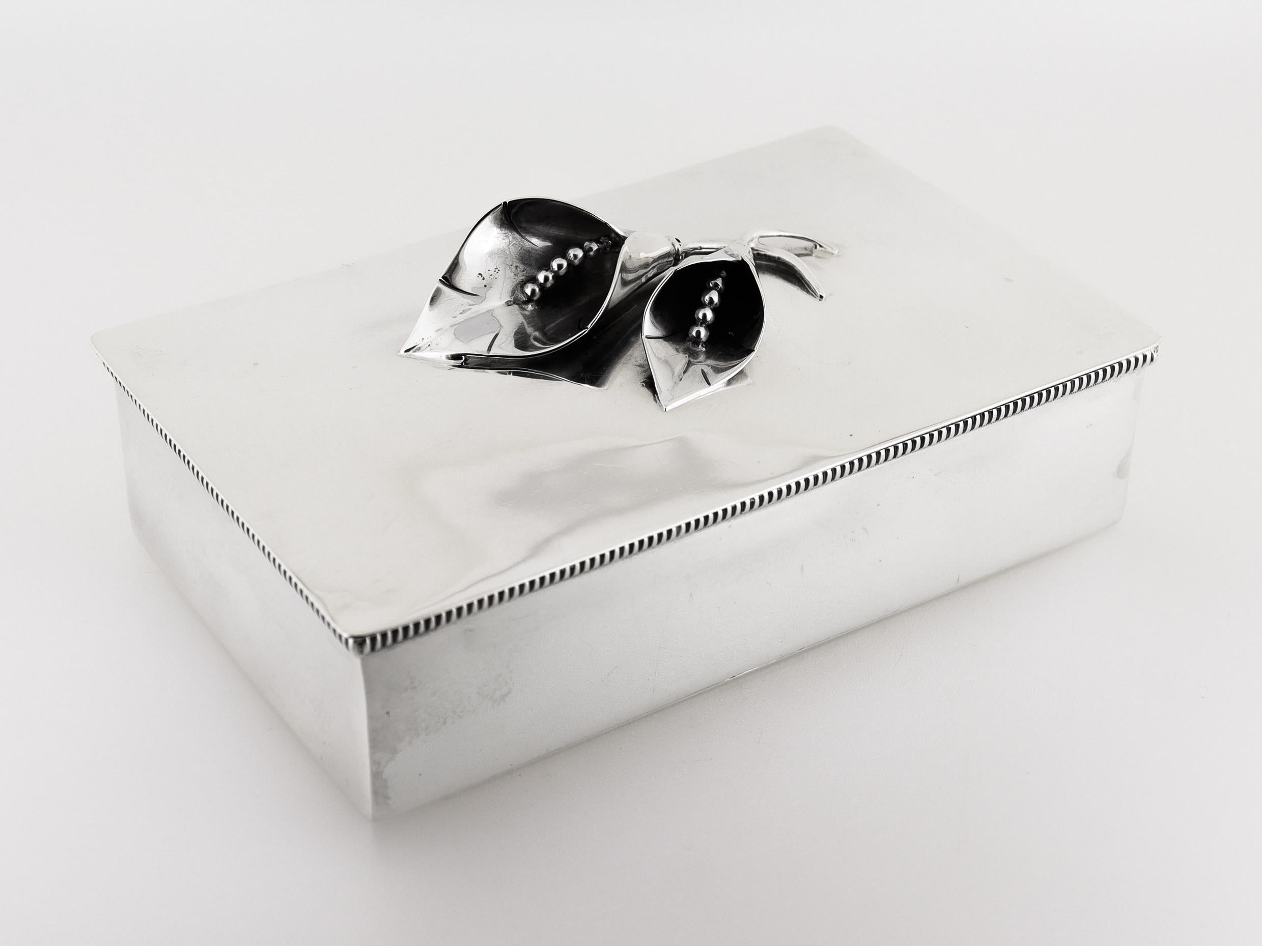A fine vintage Mid-Century Modern silver box.

In sterling silver.

By William DeMatteo. 

The lid is hinged and has two figural calla lily finials. The rim finished with a banded pattern.

Marked to the base for Sterling / Handmade / 5.

Simply a