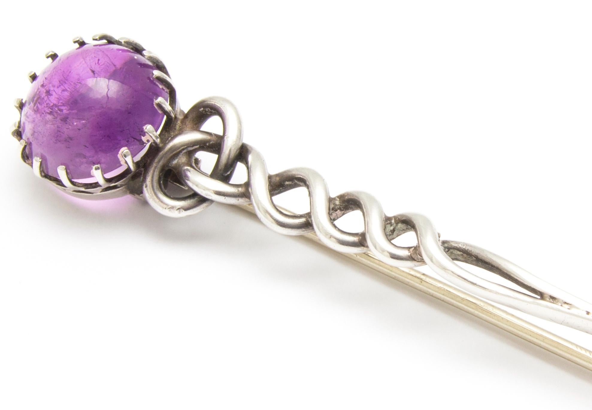 From the Arts and Crafts period, and with a distinctly Celtic style, this is an elegant sterling silver brooch in a twisted rope design. It terminates with a cabochon amethyst stone of soft purple. The brooch fastens securely with a long pin on the