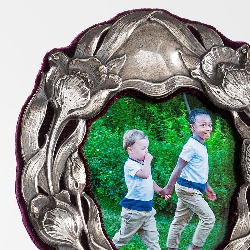 This English Art Nouveau silver picture frame, with floral decoration, by William Hutton & Sons, Ltd., features an enchanted entanglement of tulip blooms, stems and roots in relief. The roughly oval shaped frame with darling splayed feet features a