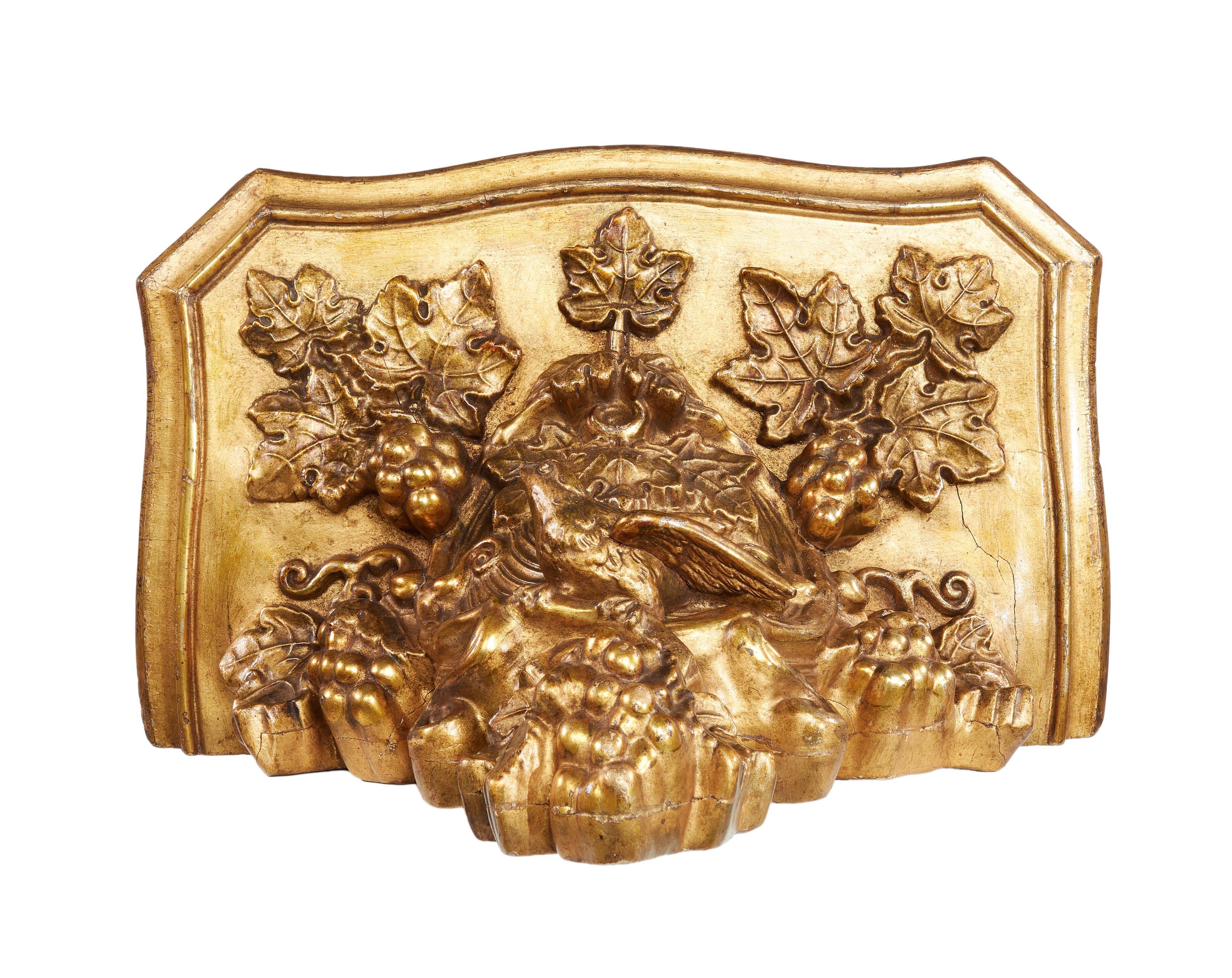 The bracket has a serpentine shaped top above a bird in it’s nest surrounded by bunches of grapes and vine leaves.
 