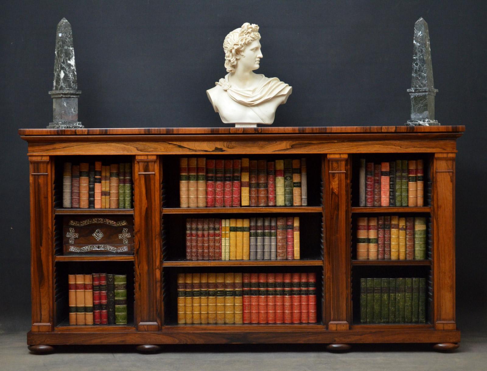 Sn4382, superior quality William IV low bookcase in rosewood, having stunning top above a three open sections with height adjustable shelves, flanked by tapering pilasters, standing on plinth base, bun feet and castors. This antique bookcase has