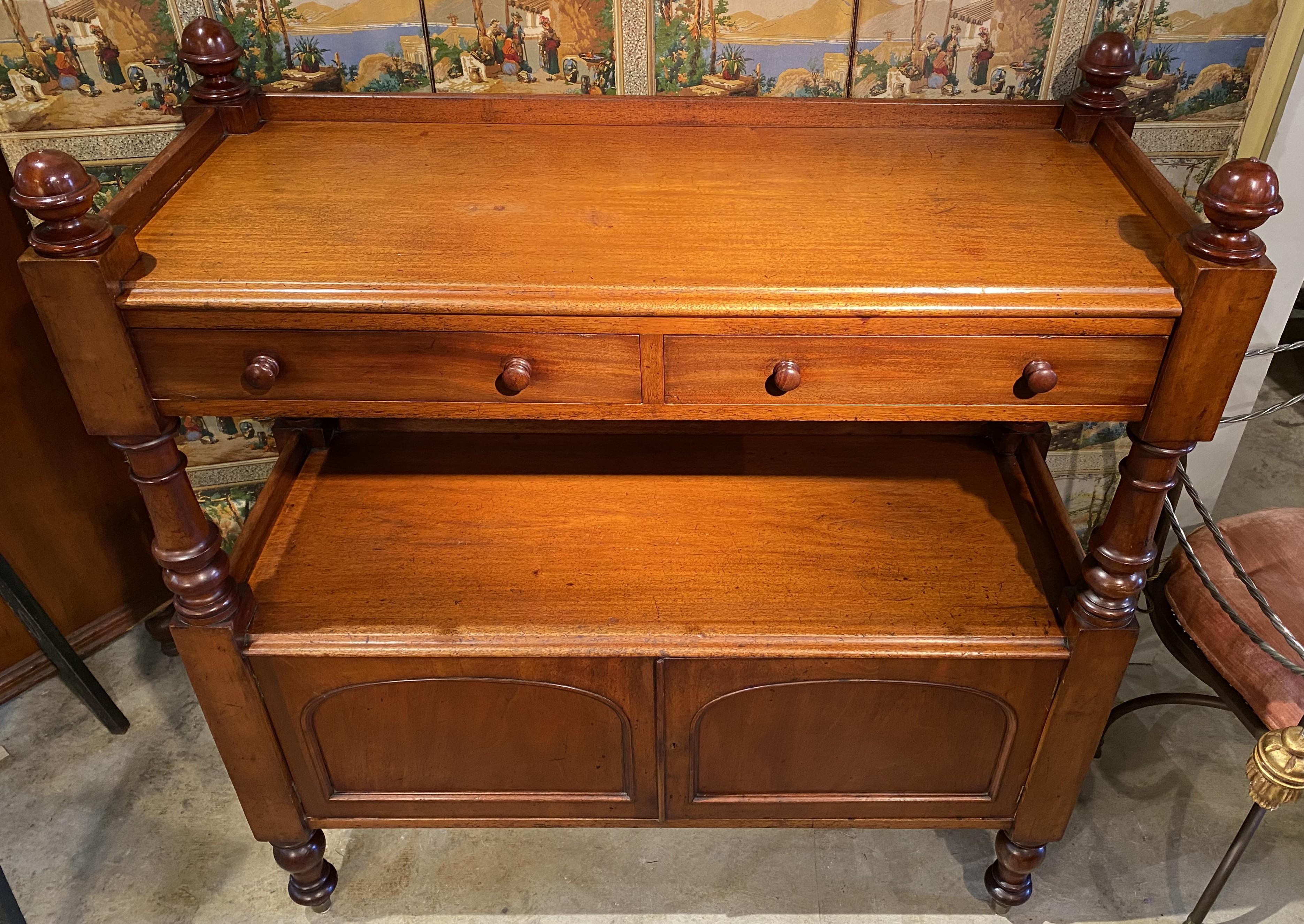 A nice form William IV English mahogany two tier server with gallery, corner ball finials, two frieze drawers, and lower cabinet with arched panel doors, opening to two adjustable drawers, all supported by four turned legs. This server dates to the
