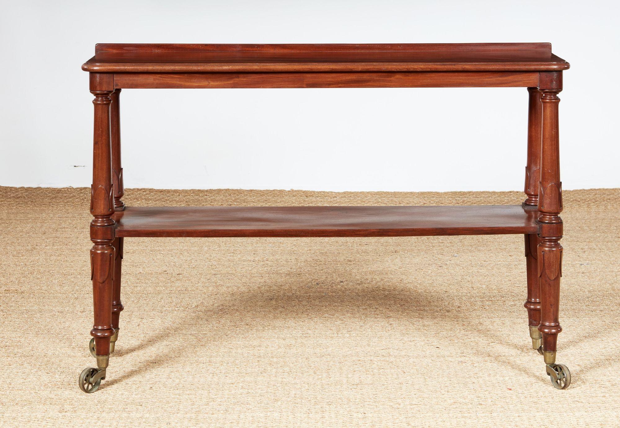 A William IV two-tier etagere in richly patinated mahogany having a top shelf with molded edge and raised back rim above integrated mid-level shelf on shaped and acanthus carved columns with turned rings above bold brass castors.
England, circa 1840.