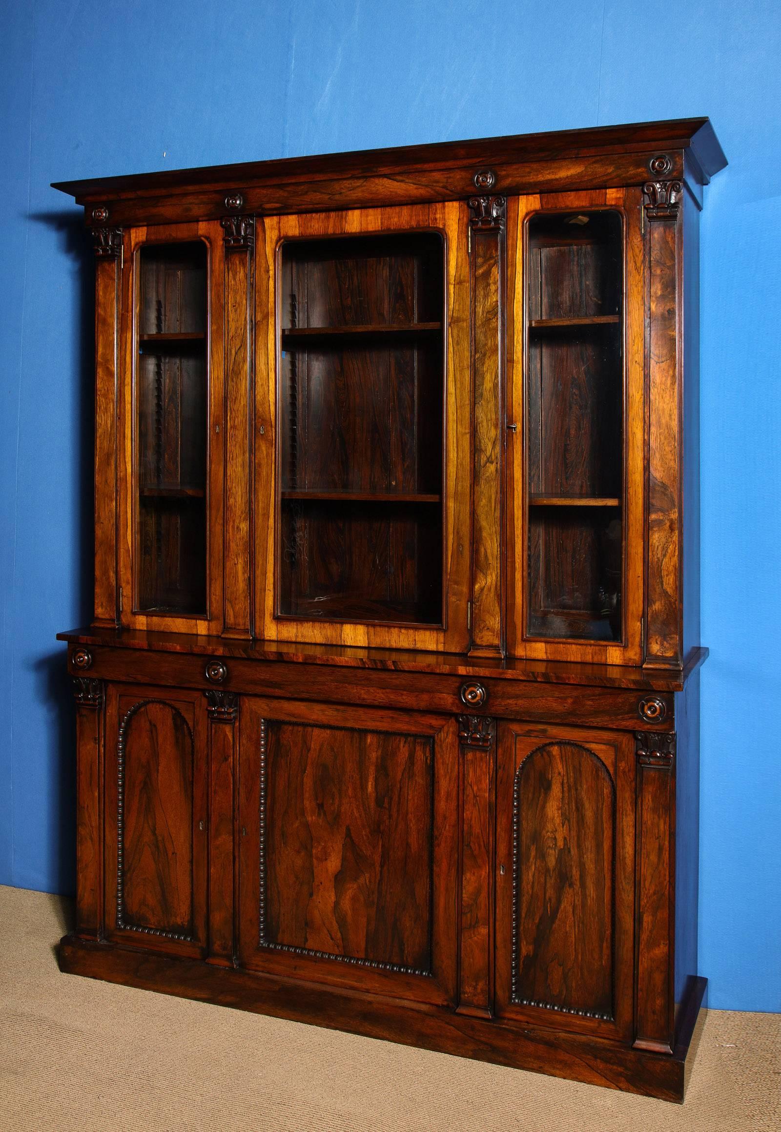 William IV  Richly Figured Rosewood Bookcase Cabinet with Book-Matched Veneers, the projecting cornice above a plain frieze adorned with finely carved applied flower heads.  The upper section with three glazed doors opening to a faux rosewood