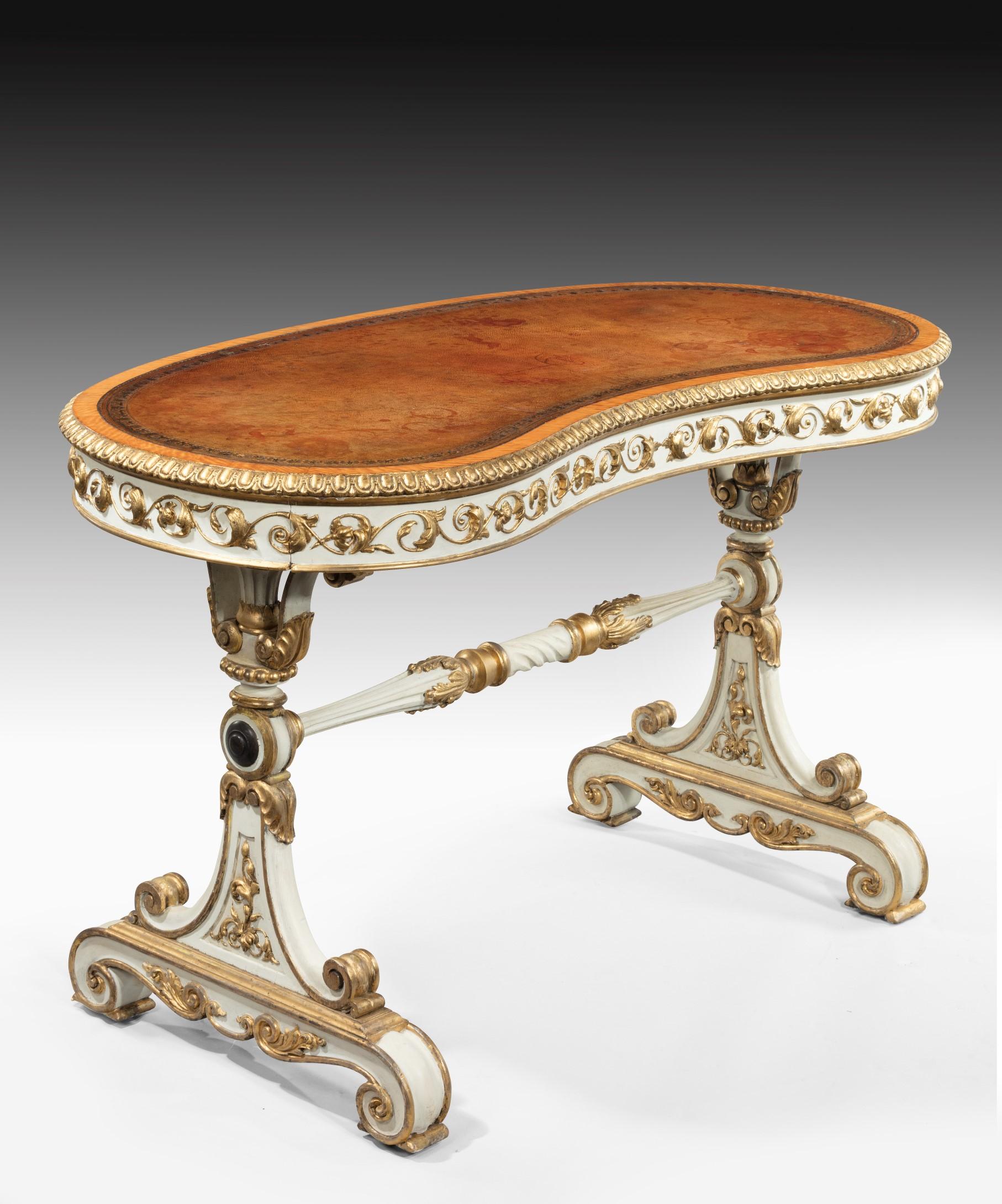 A rare William IV period kidney shaped writing table with carved giltwood decoration and white paintwork: the writing table's leathered top crossbanded in satinwood and with a carved gadrooned edge above a frieze composed of scrolling acanthus