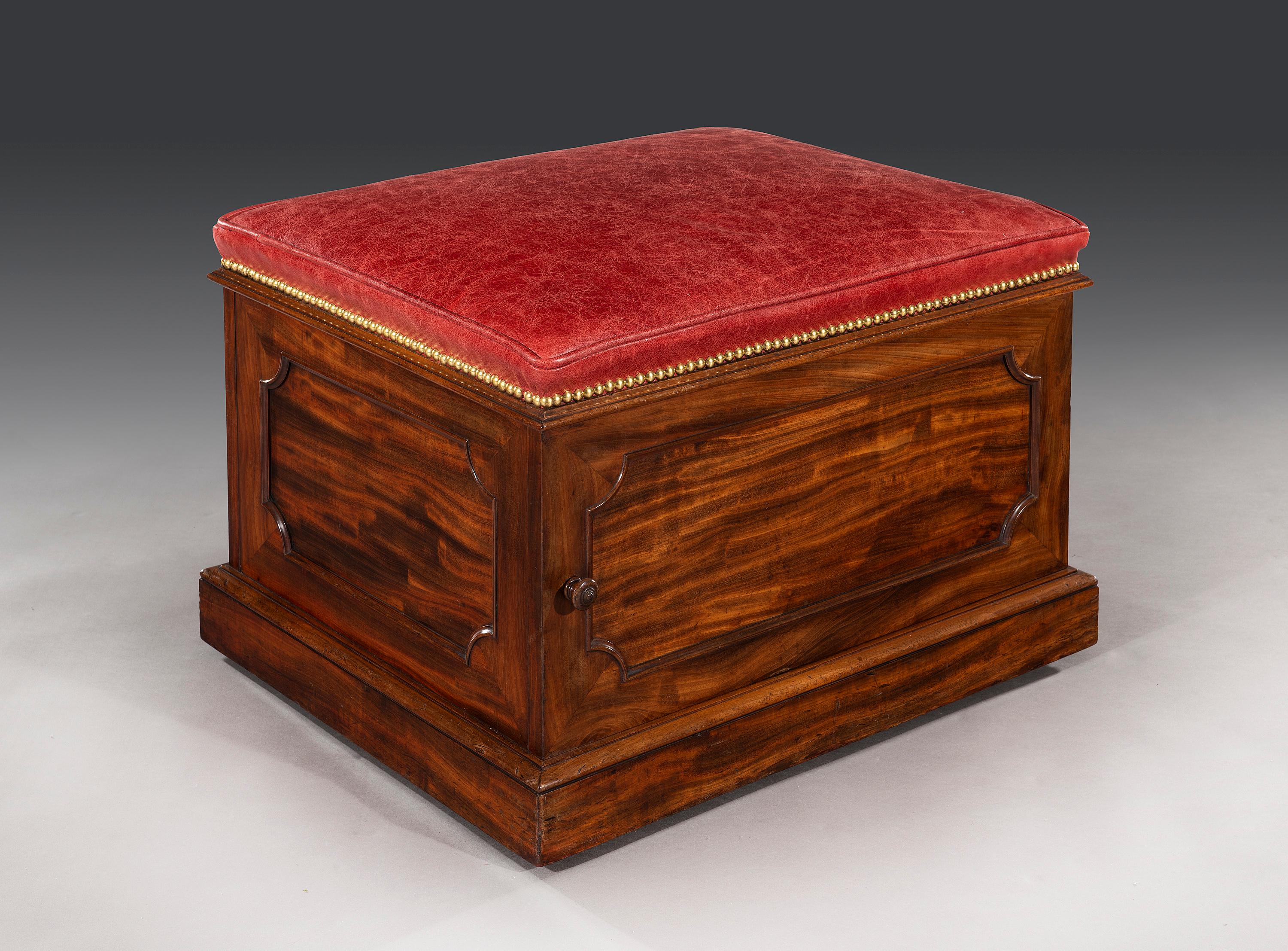 A good William IV mahogany and leather box stool of unusual form; by Doveston Bird and Hull. The rectangular padded seat, newly upholstered in good quality red hide with a piped edge and close brass studs, above a shaped mahogany molding. The door
