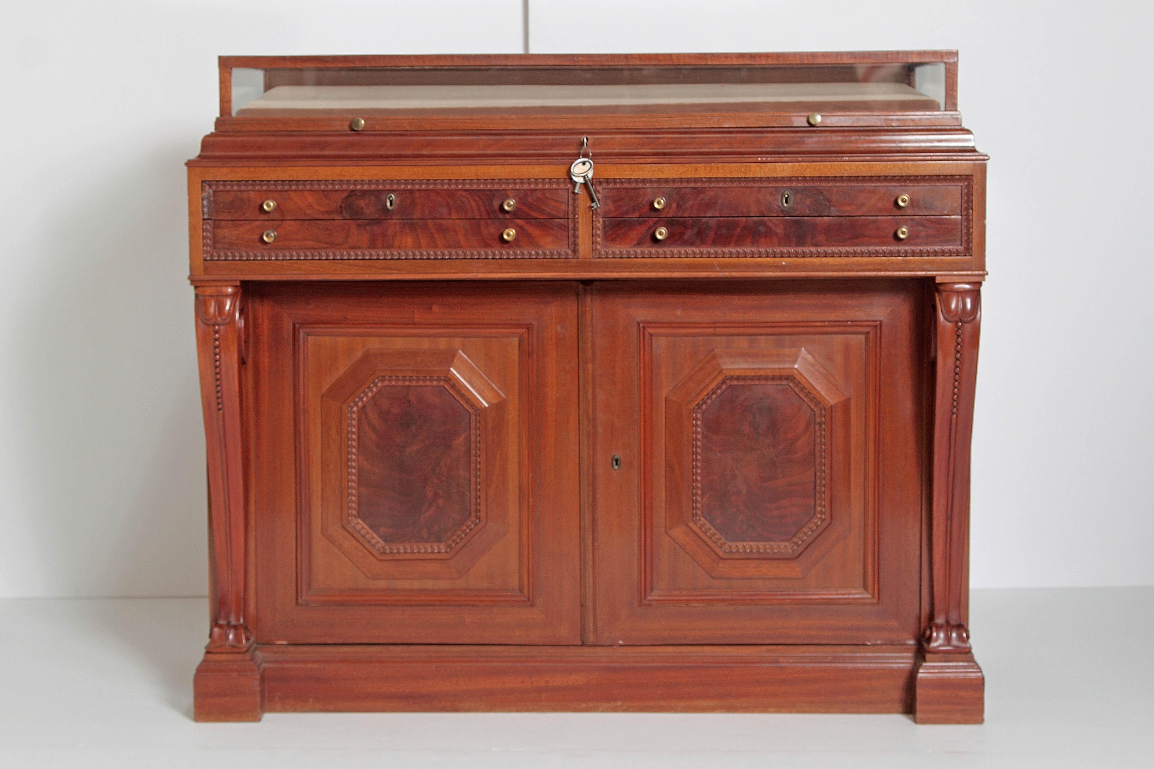 An English mahogany cabinet with a glass display / vitrine top with key, above: four lined locking drawers for silver / jewlery storage and below: a cabinet with two doors that open to a single shelf. The drawers and cabinet doors have elegant