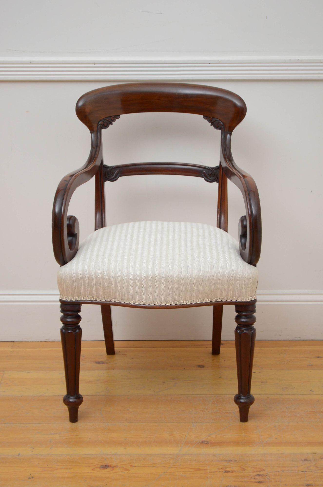 J030 Elegant William IV elbow chair in mahogany, having shaped top rail with decorative carved motifs below, carved mid rails, open scroll arms and generous seat, all standing in fluted legs. This antique armchairs is in home ready condition.