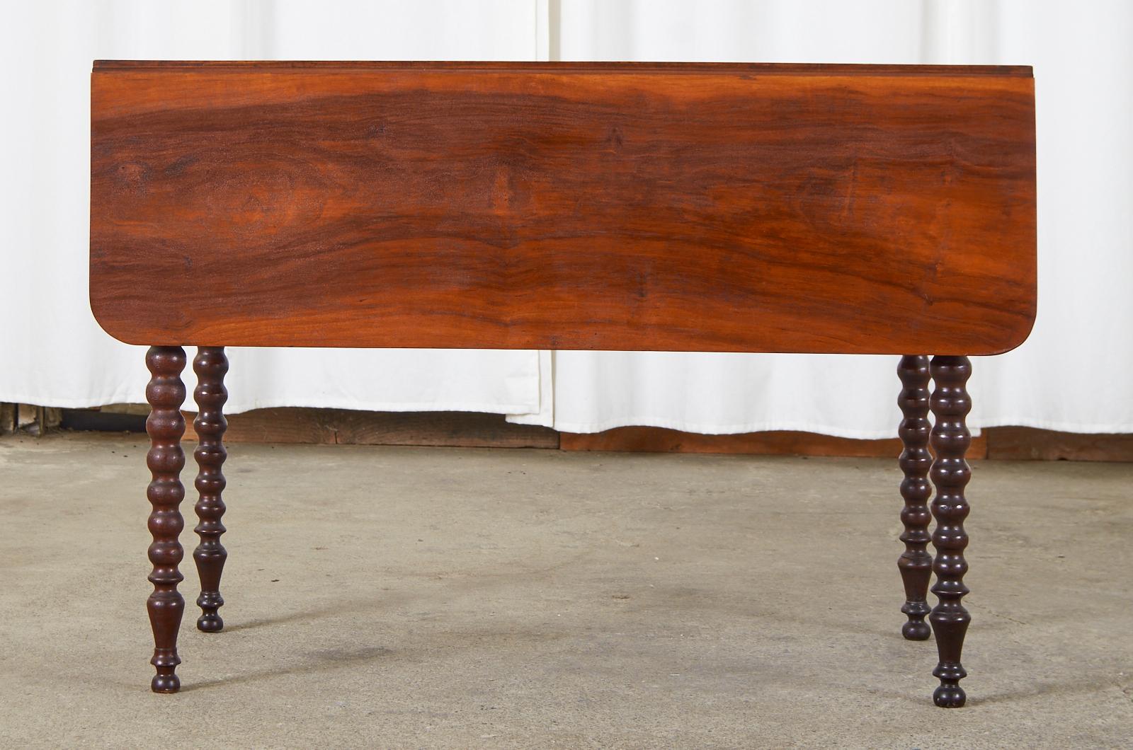 Handsome English 19th century mahogany drop-leaf dining table or Pembroke table. Made in the William IV taste featuring spindle legs or bobbin turned legs and ending with ball feet. The plank top measures 42 inches wide with the leaves open and 20