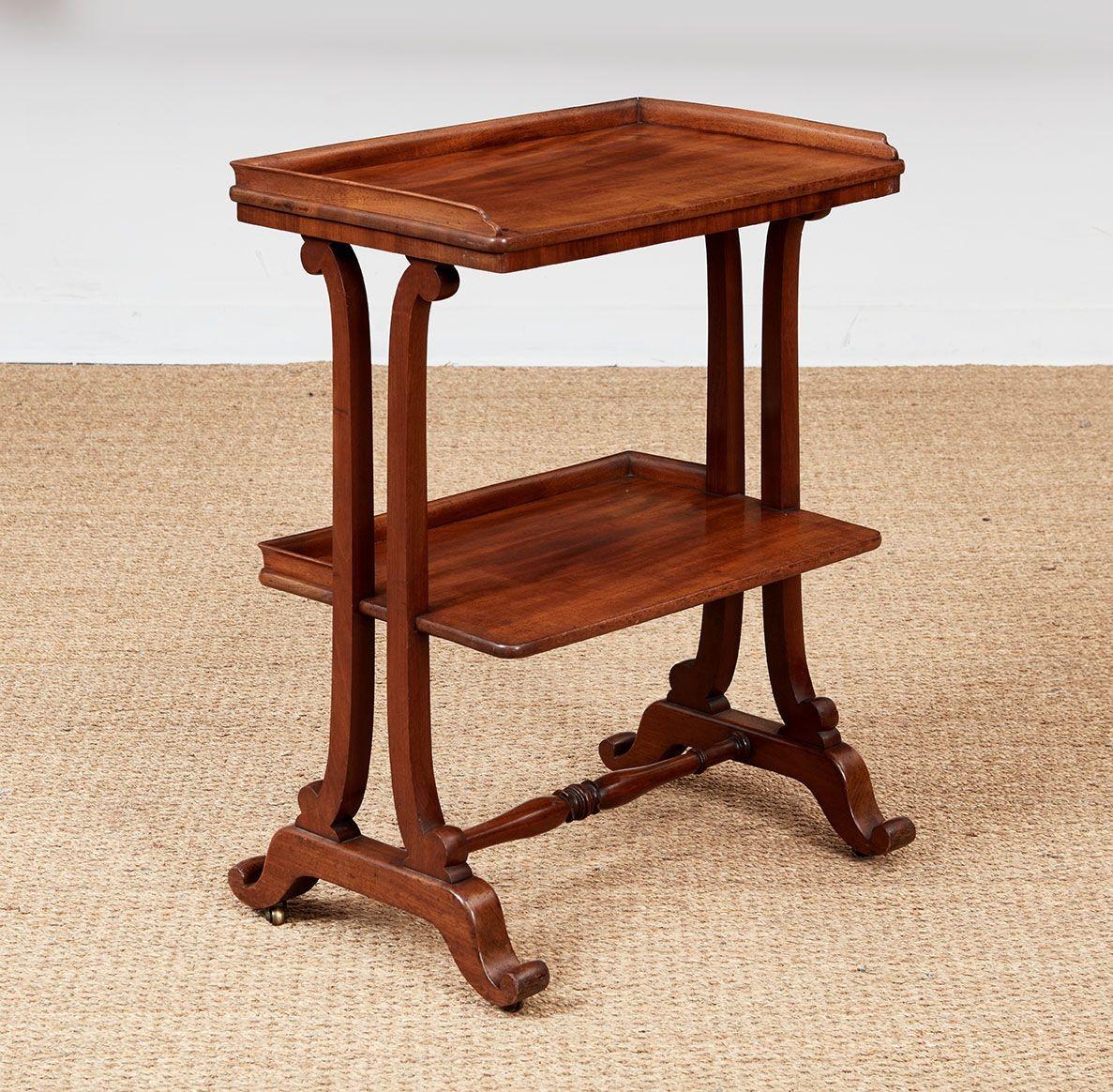 A William IV etagere in choice mahogany having graceful lines with two vertical curved braces supporting an upper and a lower shelf, each with raised borders, all on conforming brace feet with rolled ends joined by a turned stretcher.  English,