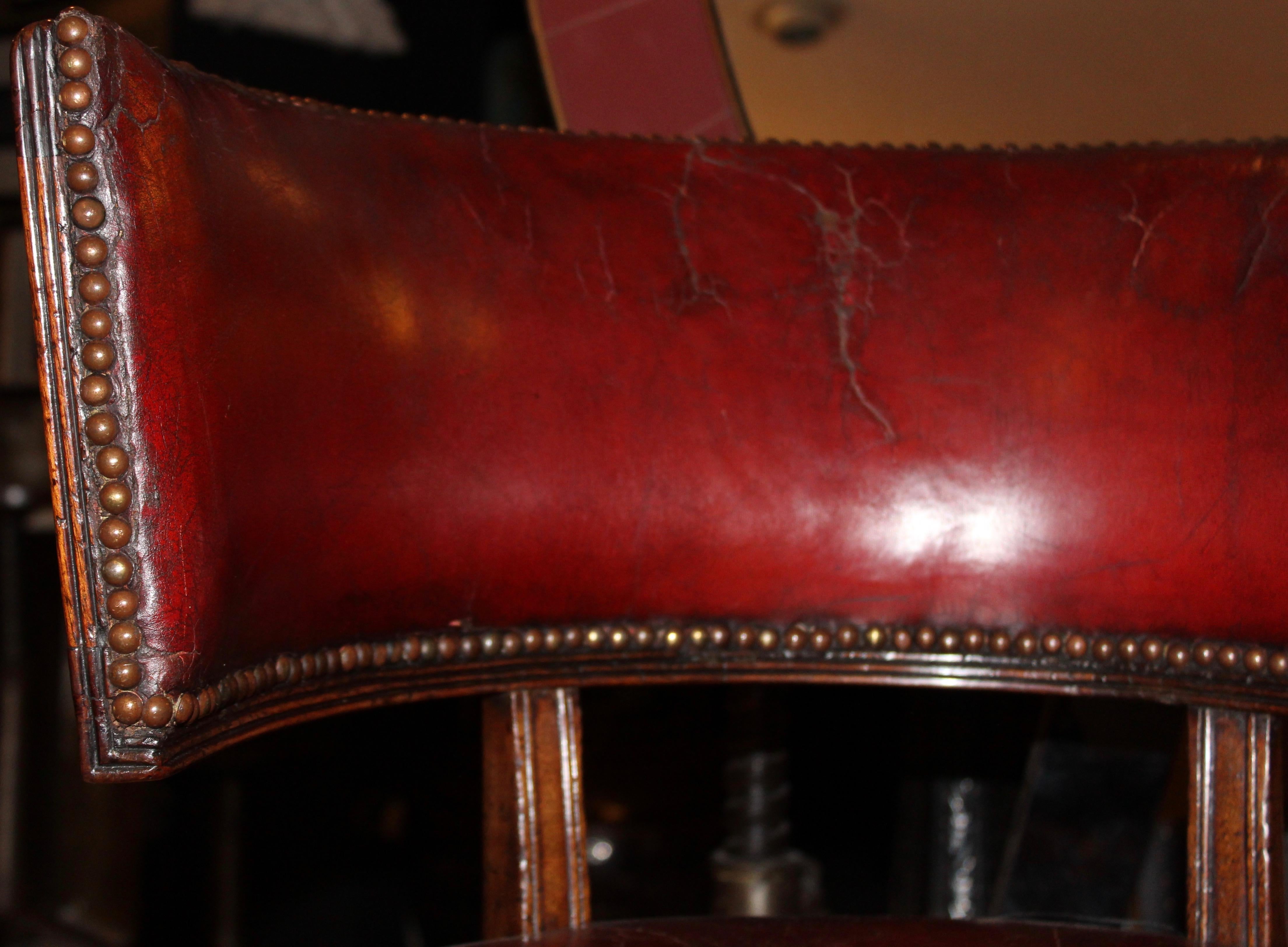 English William IV mahogany and aged red leather Klismos style desk chair, circa 1840. With turned tapered front legs and outwardly curved back legs. The aged red leather upholstery affixed with brass studwork. The curved back with further red
