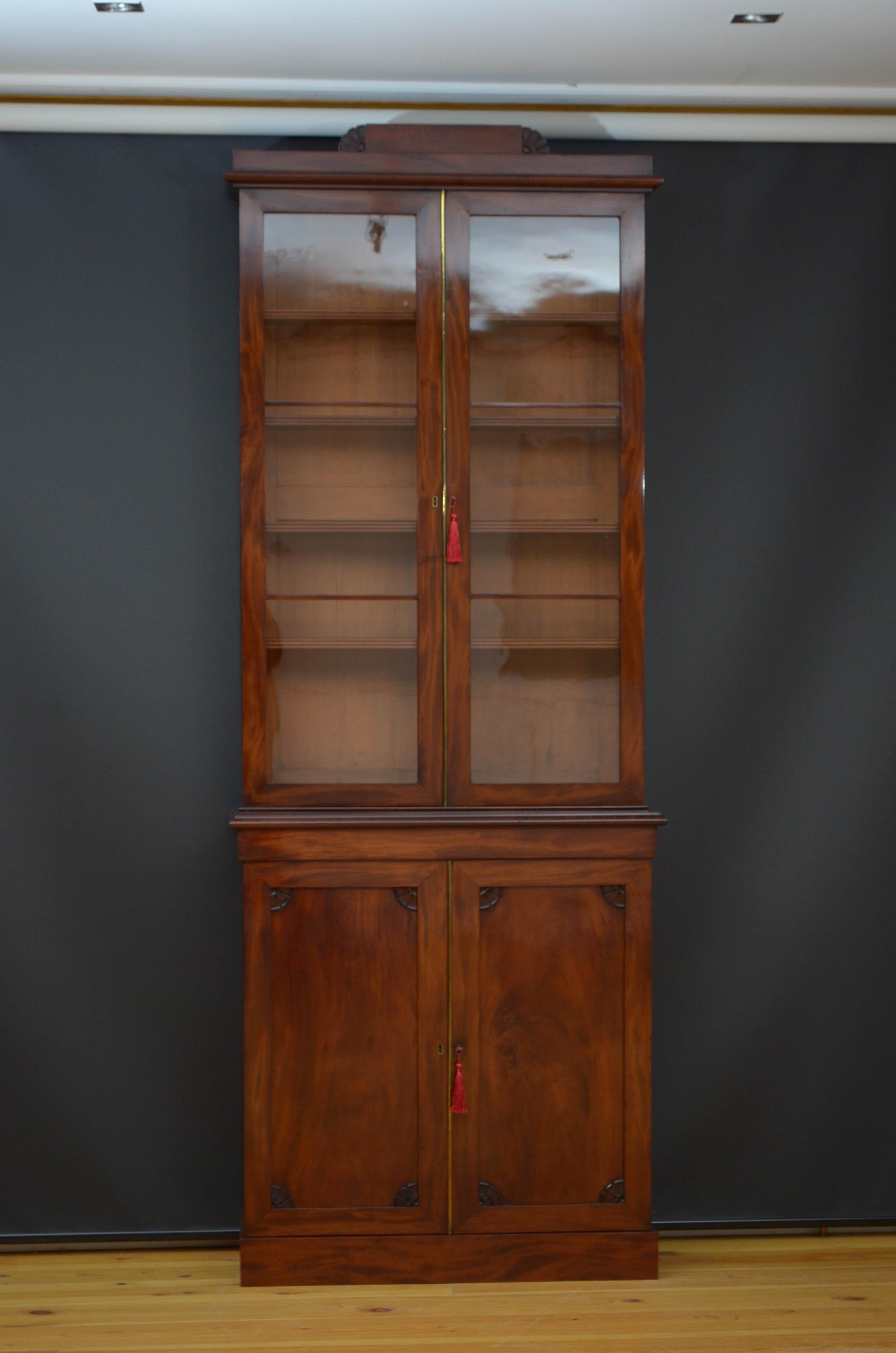 Sn5141 Tall and slim William bookcase in mahogany, having carved pediment to moulded cornice above a pair of glazed doors fitted with original working lock and a key and enclosing four height adjustable shelves, the projecting base having a pair of