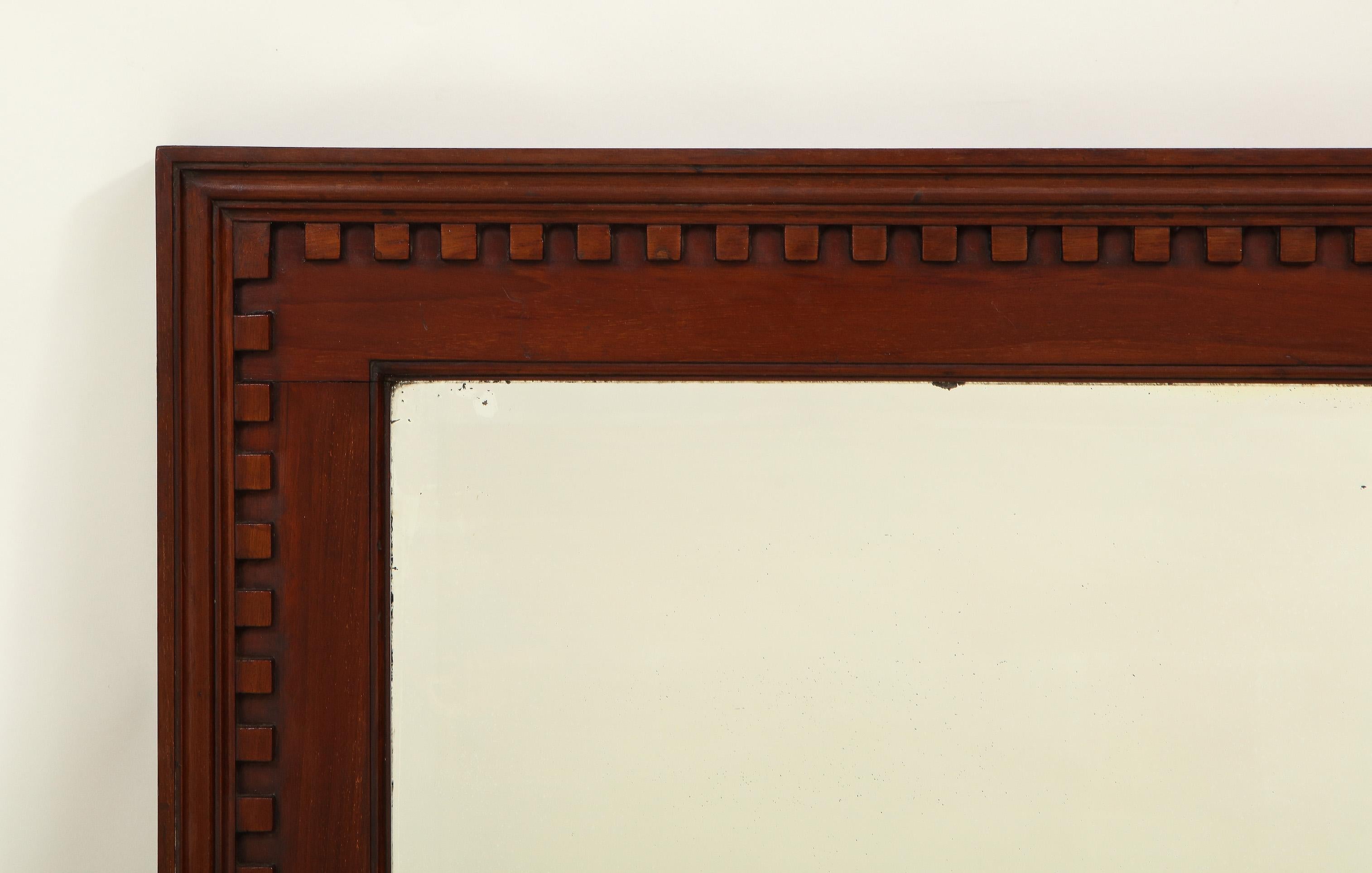 The beveled rectangular mirror plate within a conforming solid mahogany frame, boldly carved with dentil banding. Handsome piece.